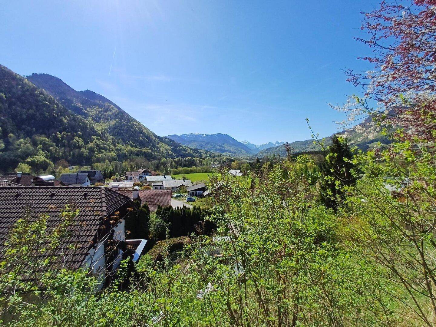 Panoramablick über eine ländliche Siedlung mit grünen Hügeln und majestätischen Bergen am Horizont.