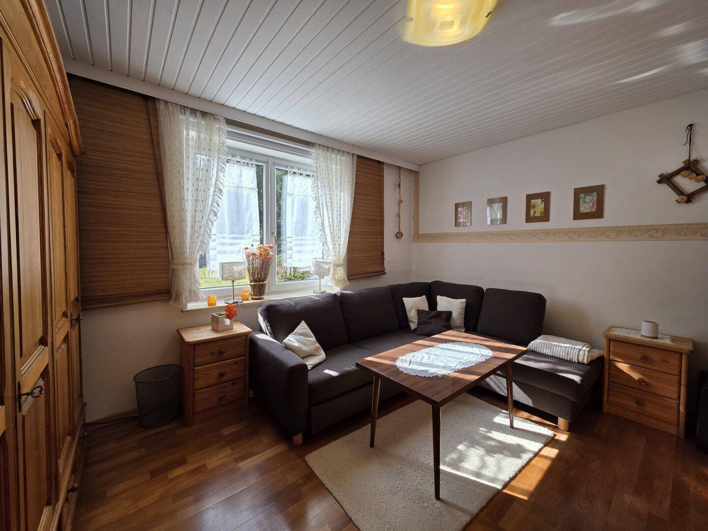 Gemütlicher Wohnbereich mit Ecksofa, Holzboden und Blick in den Garten.
