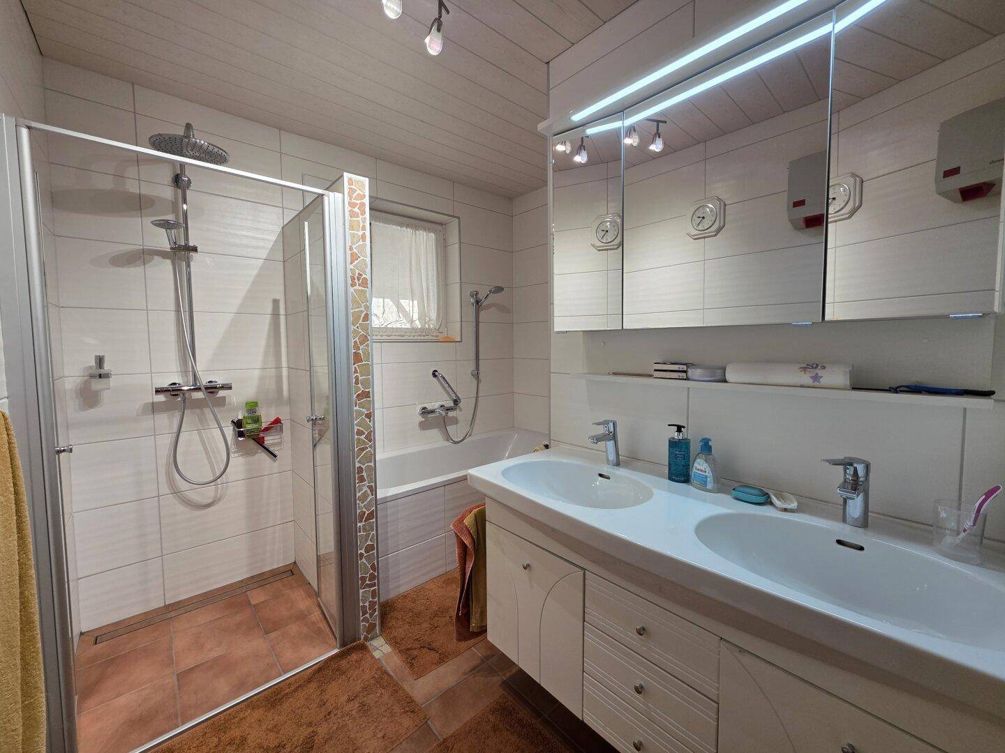 Modernisiertes Badezimmer mit Doppelwaschbecken, Dusche und Badewanne, hell gefliest.