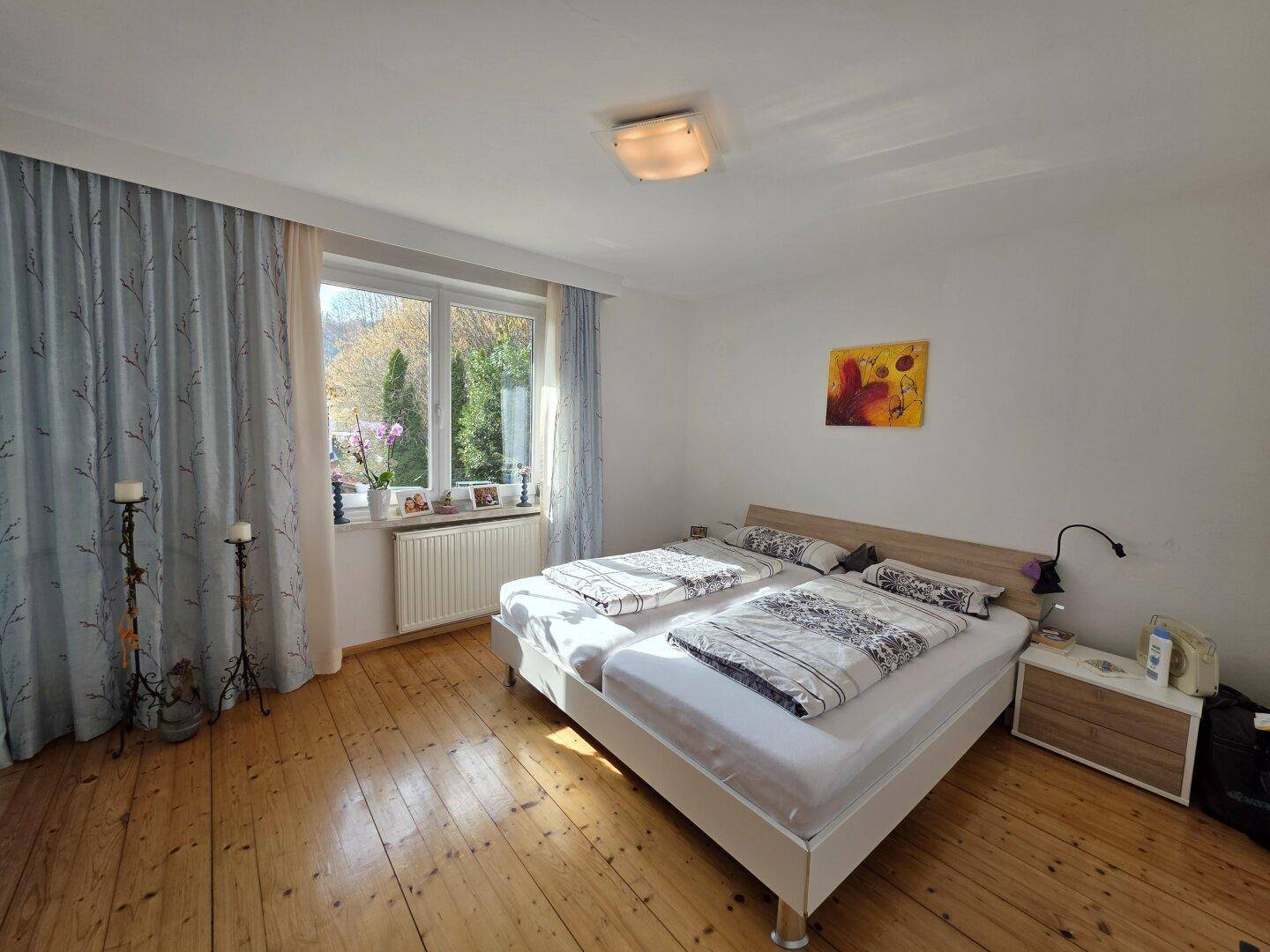 Helles Schlafzimmer mit Holzboden, Doppelbett und Blick ins Grüne.