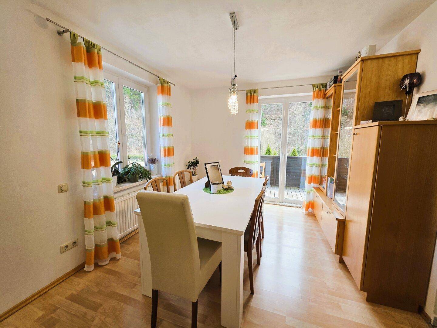Heller Essbereich mit großem Esstisch, Holzboden und Zugang zu einem Balkon.