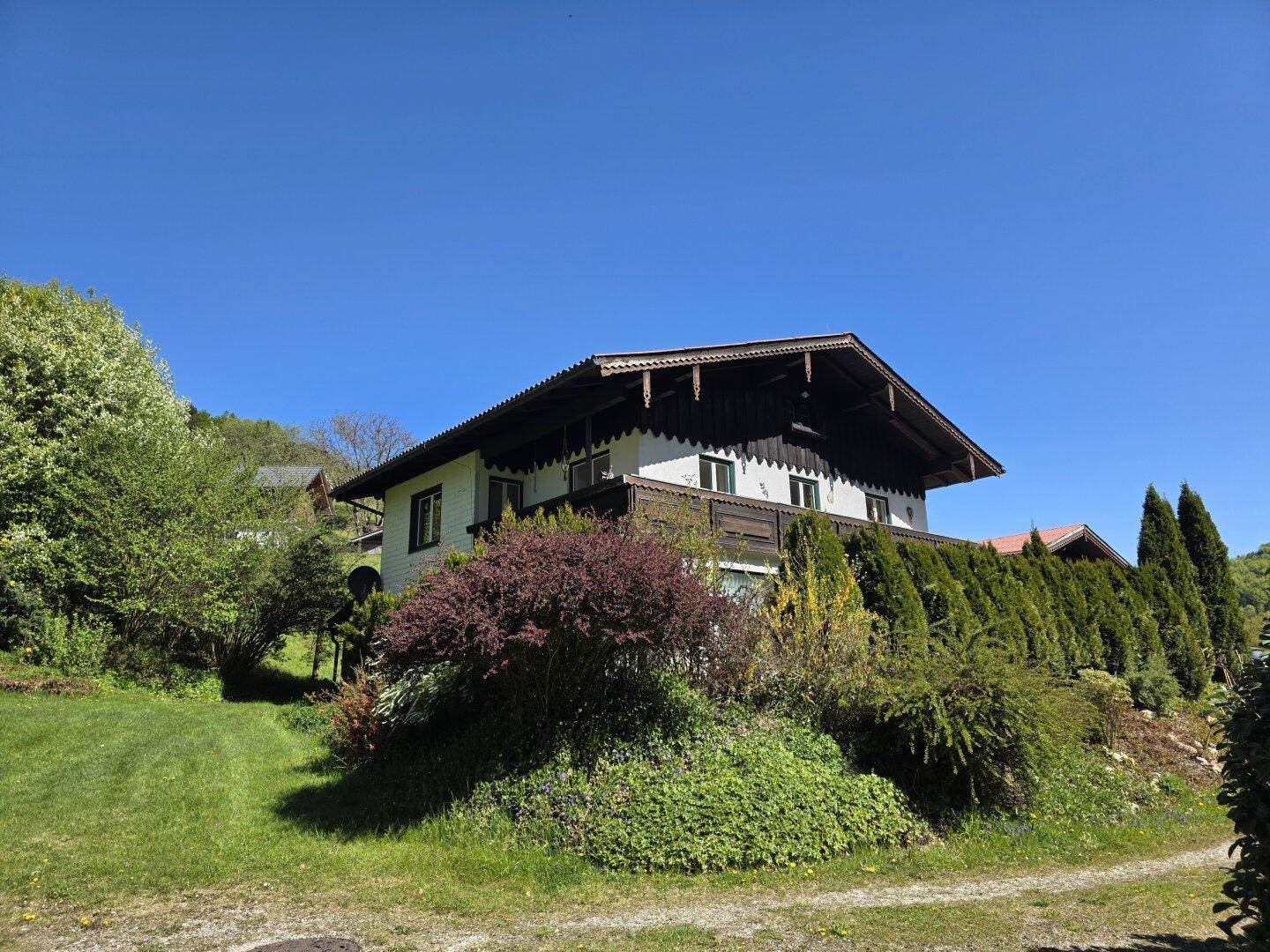 Traditionelles Landhaus mit Holzbalkonen und gepflegter Bepflanzung am Hang.