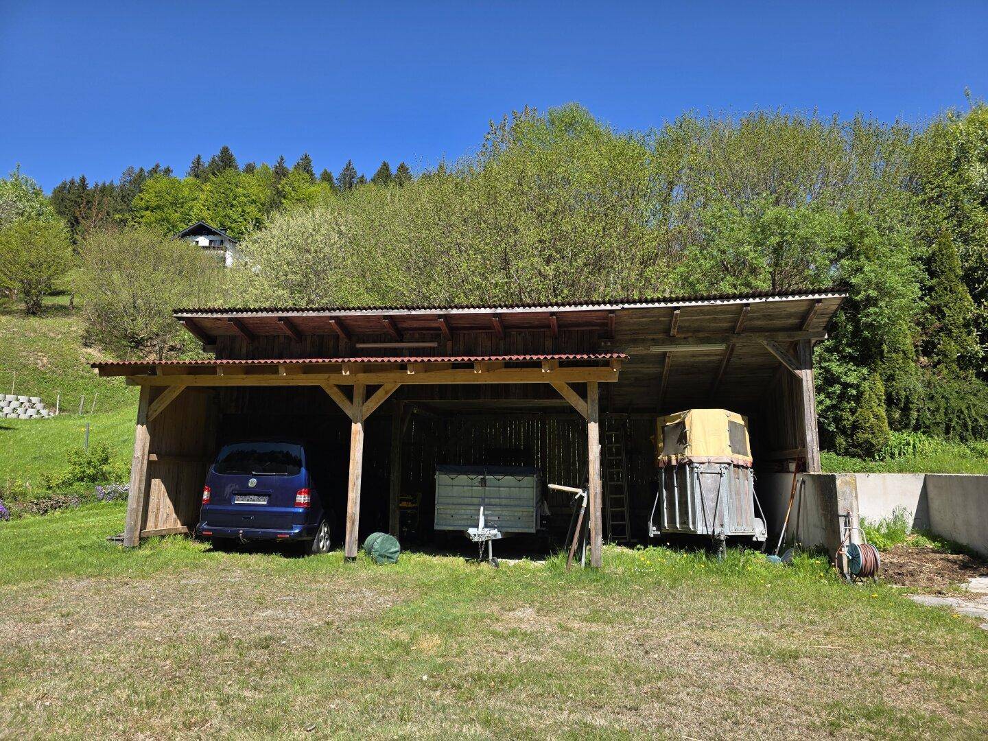 Überdachter Unterstand für Fahrzeuge und Geräte, umgeben von grüner Landschaft.