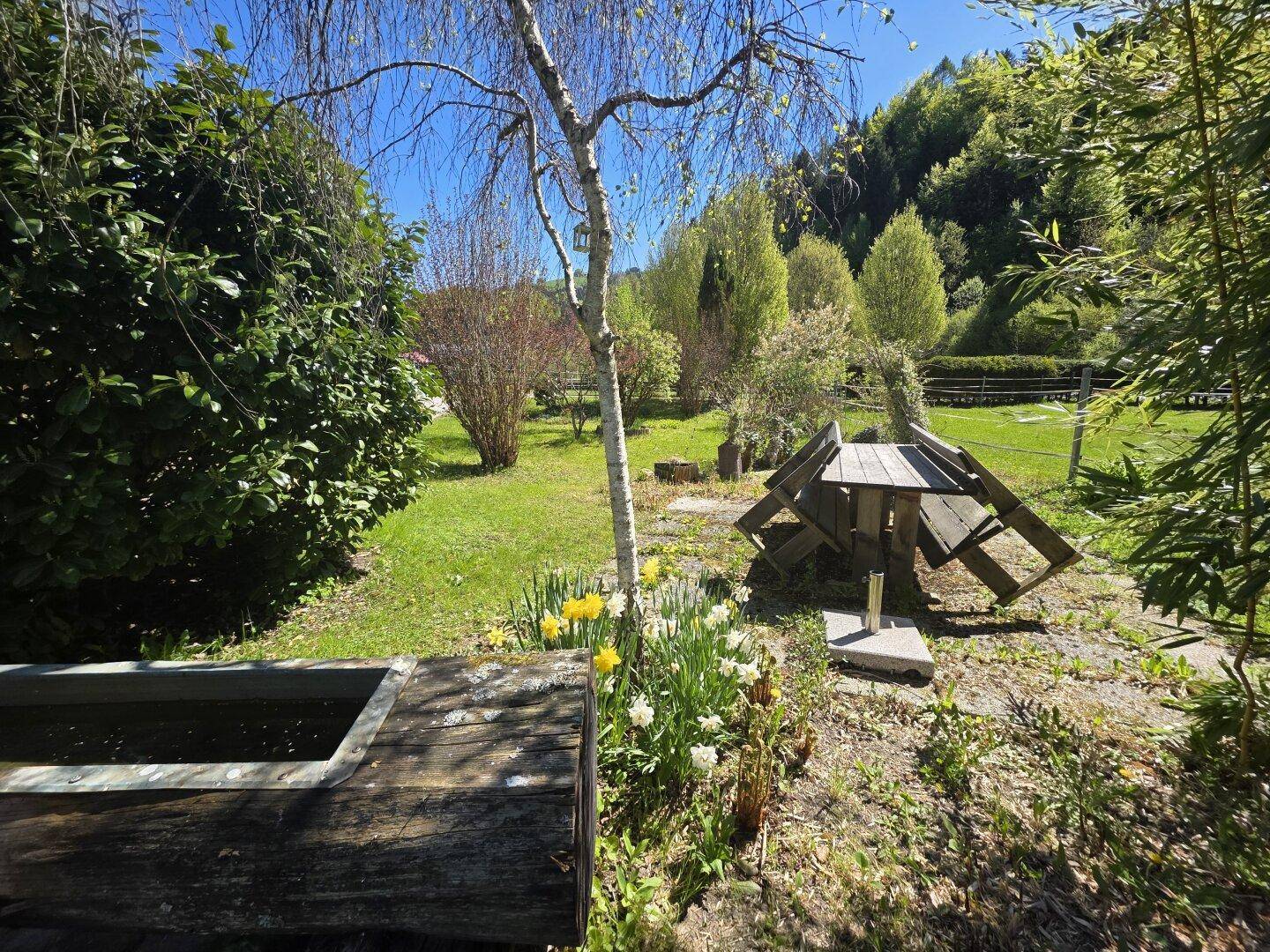 Idyllischer Gartenbereich mit Holzbrunnen, Blumenbeeten und altem Baumbestand.