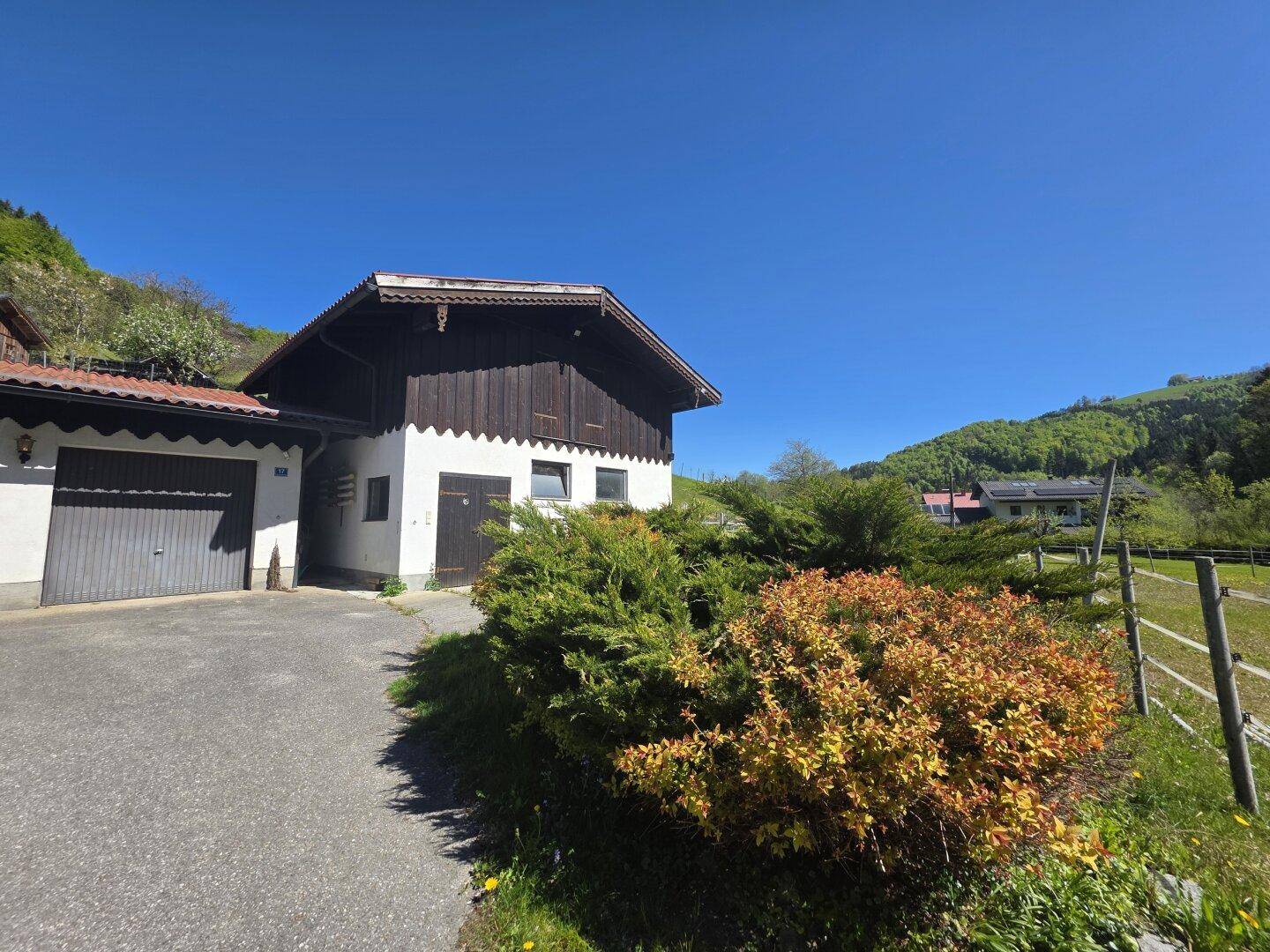 Nebengebäude mit traditioneller Holzfassade und angrenzender Garage in sonniger Lage.