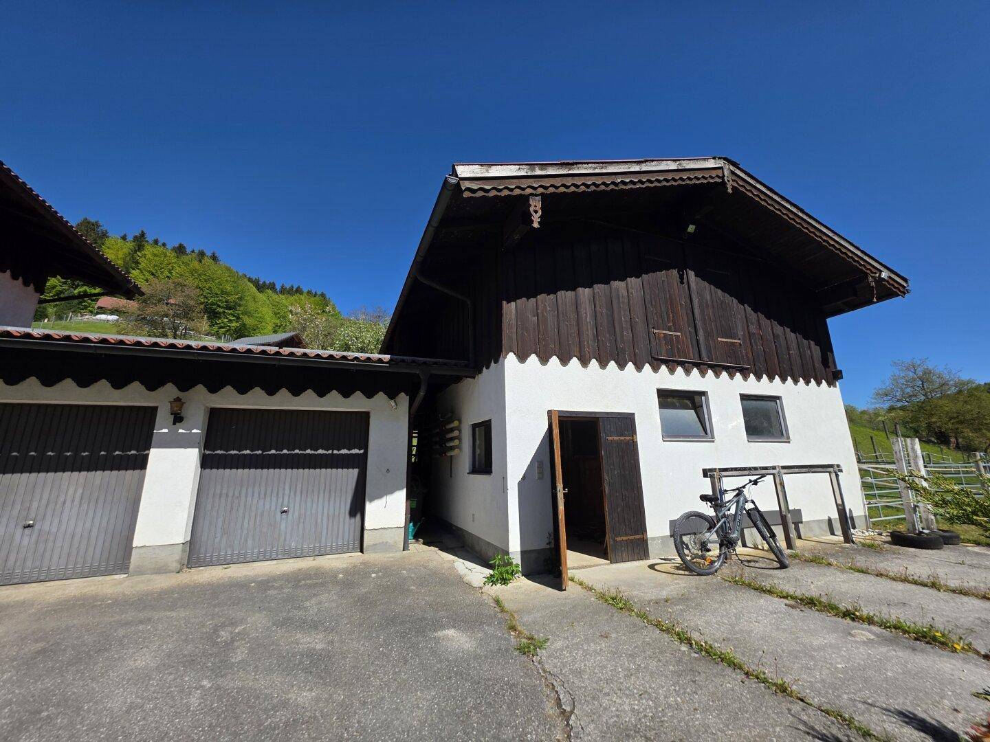 Nebengebäude mit Holzfassade und angrenzender Garage, umgeben von ländlicher Natur.