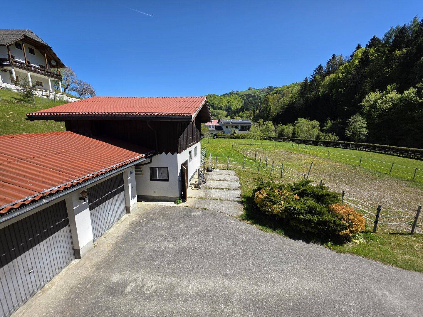 Nebengebäude mit Doppelgarage und traditionellem Dach, umgeben von grüner Natur.