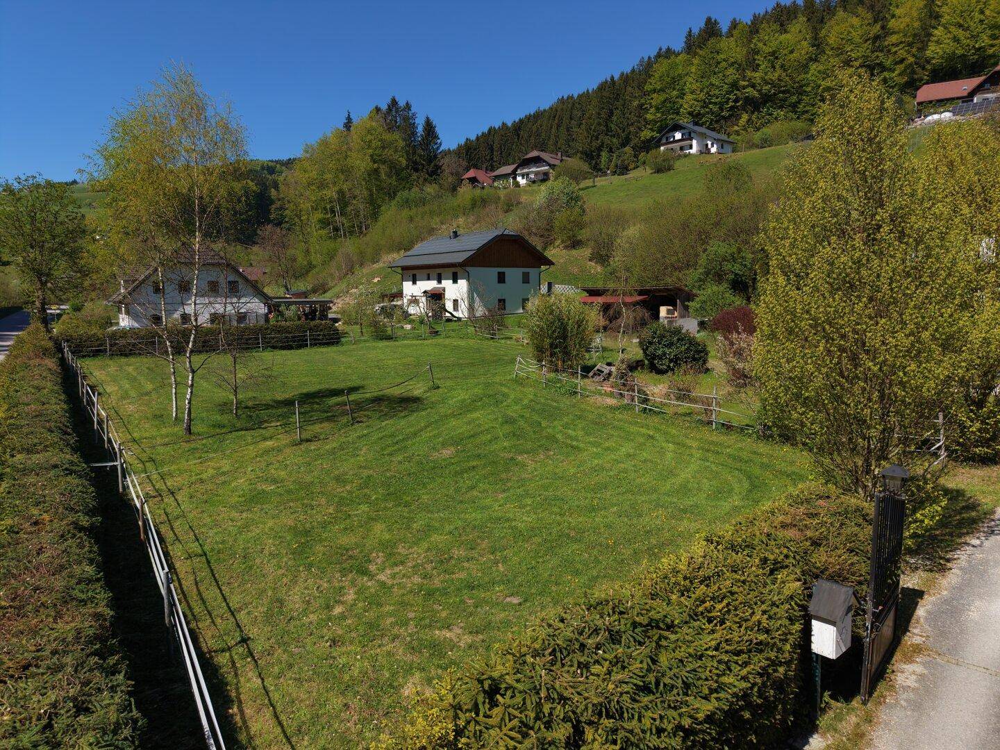 Panoramablick auf die grünen Wiesen und die umliegende Hügellandschaft mit weiteren Häusern.