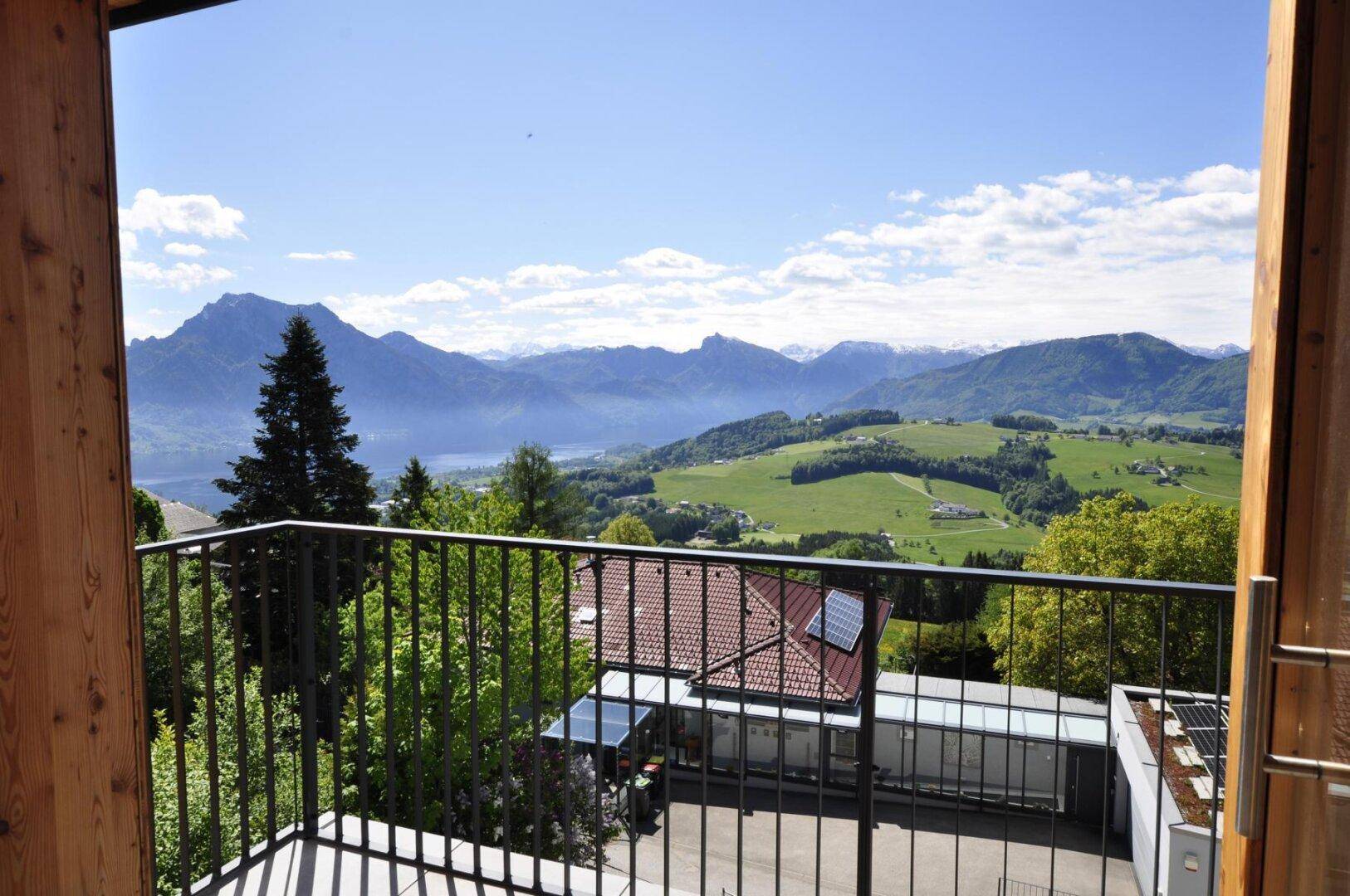 Balkon mit Fliesenboden und weitem Blick auf Berge, See und grüne Landschaft.