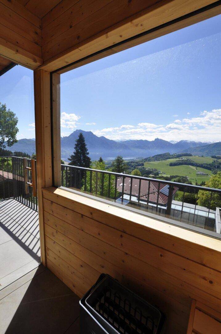 Heller Raum mit Holzverkleidung und Panoramafenstern mit Blick auf Berge und See.