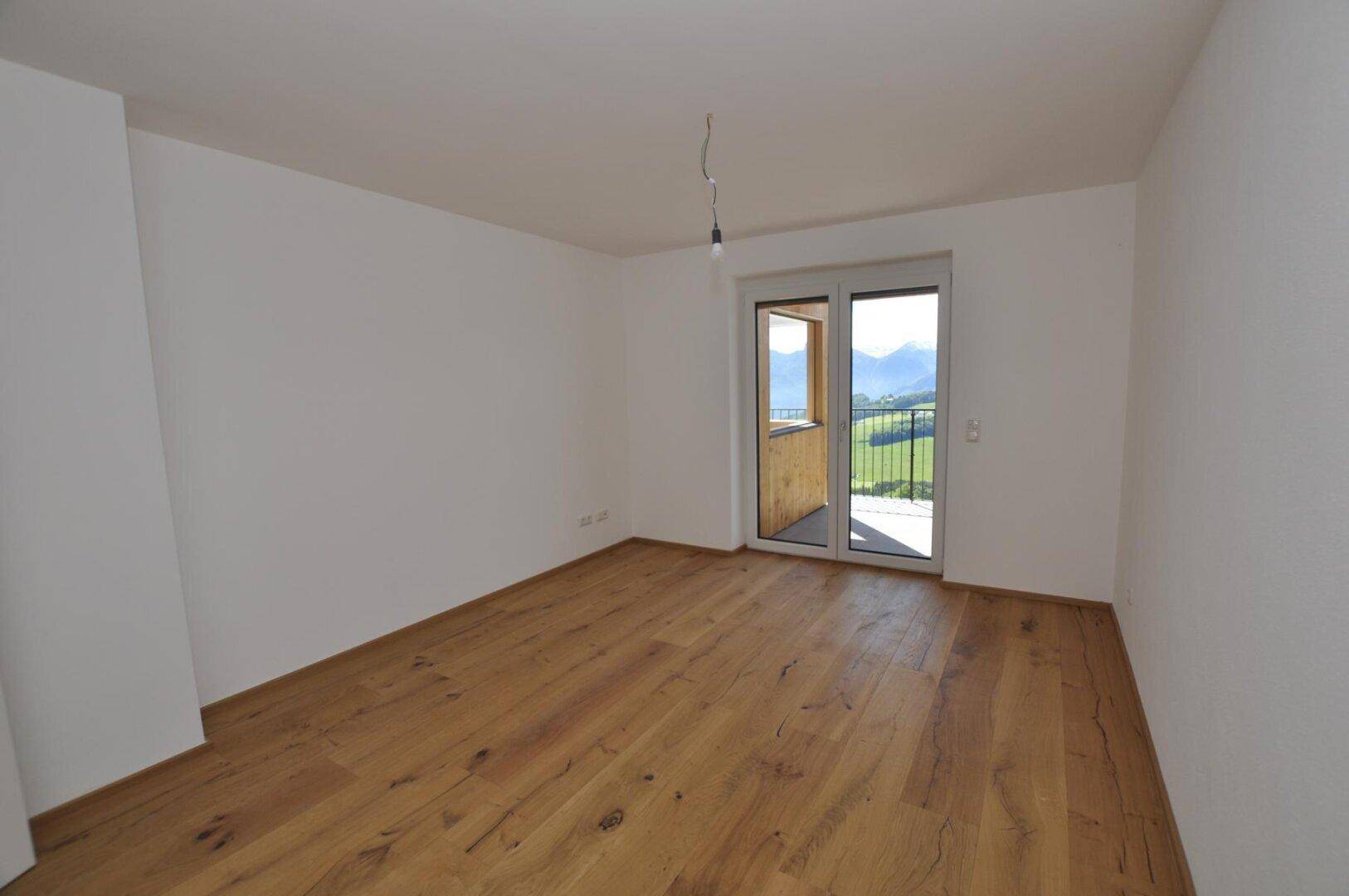 Helles Schlafzimmer mit Holzboden und Balkonzugang mit Bergblick.