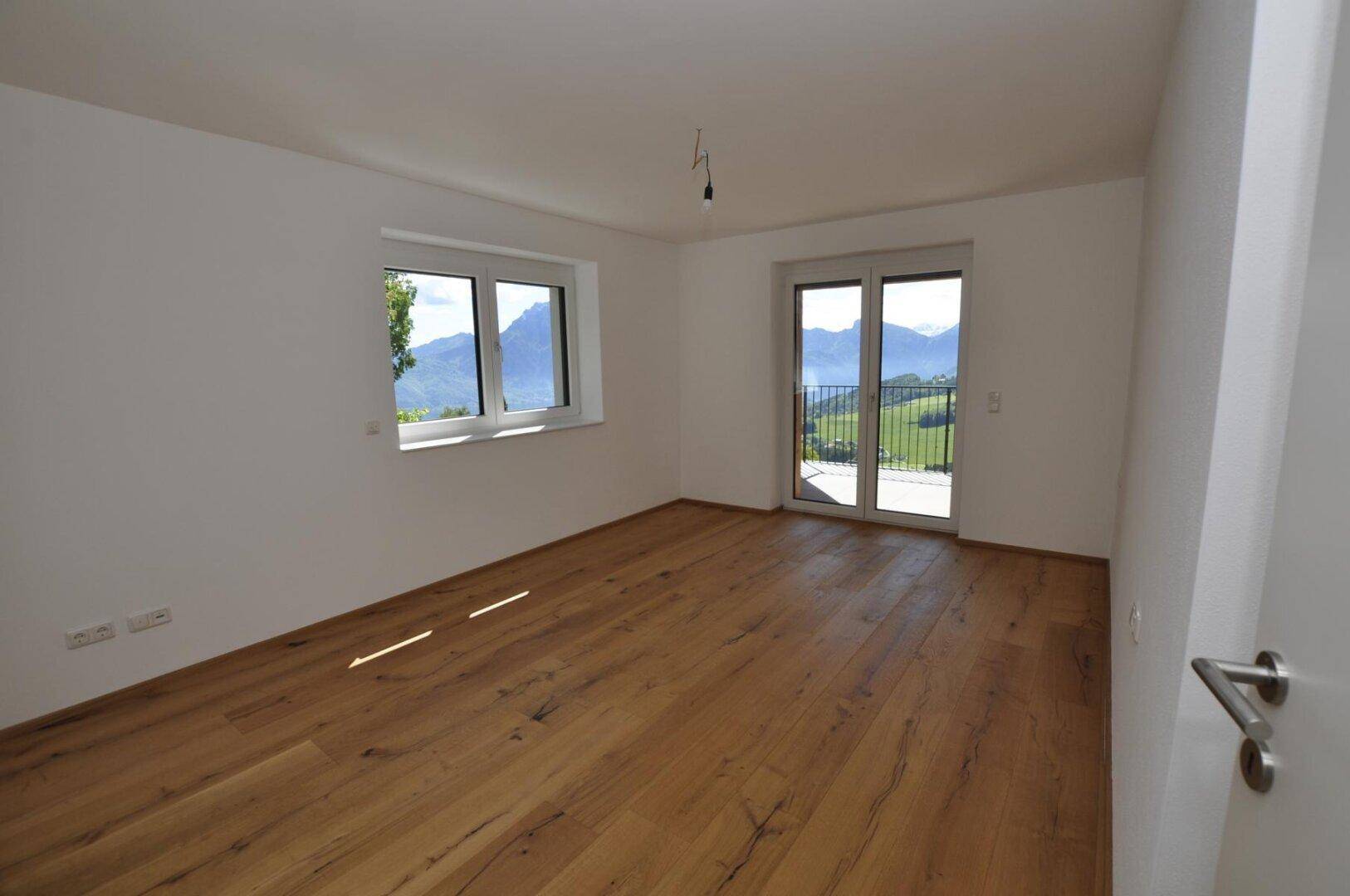 Schlafzimmer mit Holzboden und Zugang zum Balkon mit Bergblick.