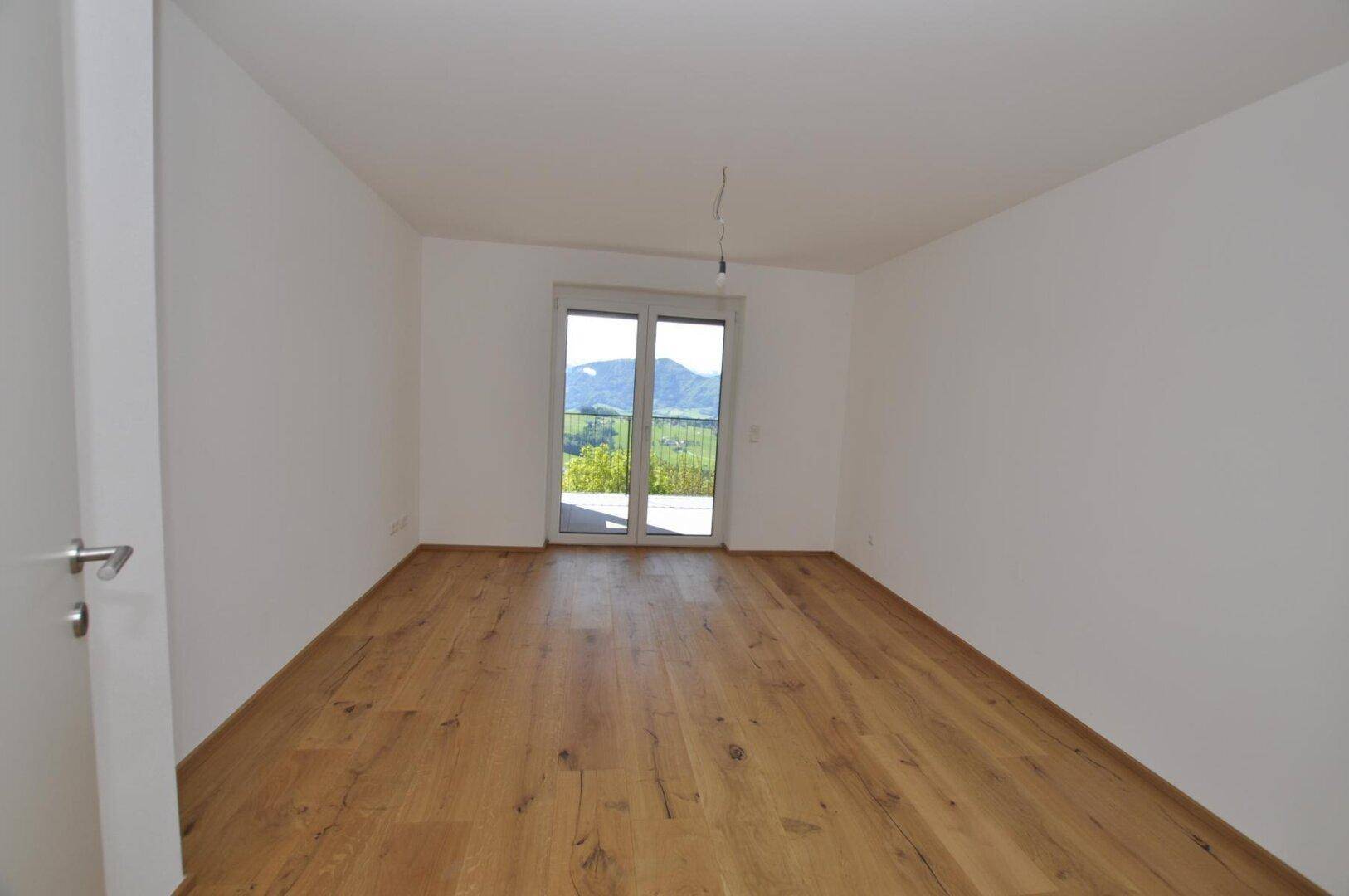 Geräumiges Schlafzimmer mit Holzboden und Balkonzugang mit Bergblick.