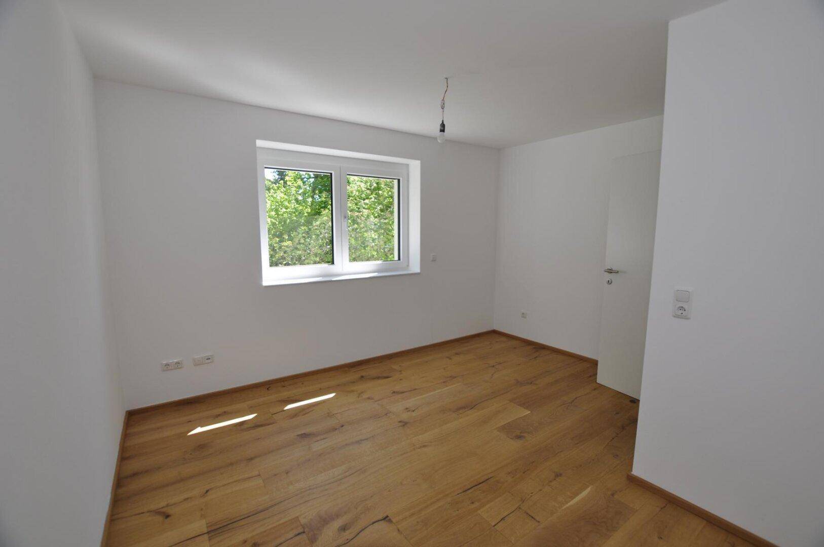 Schlafzimmer mit Holzboden und Fenster mit Blick ins Grüne.