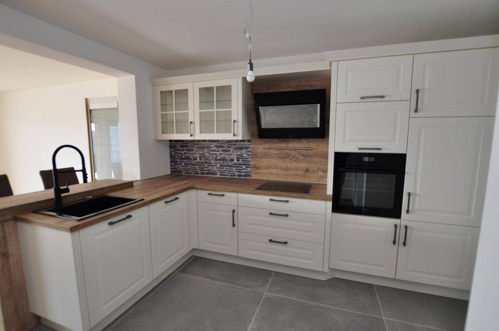 Moderne Einbauküche in Weiß mit Holz-Arbeitsplatten und integrierten Geräten.
