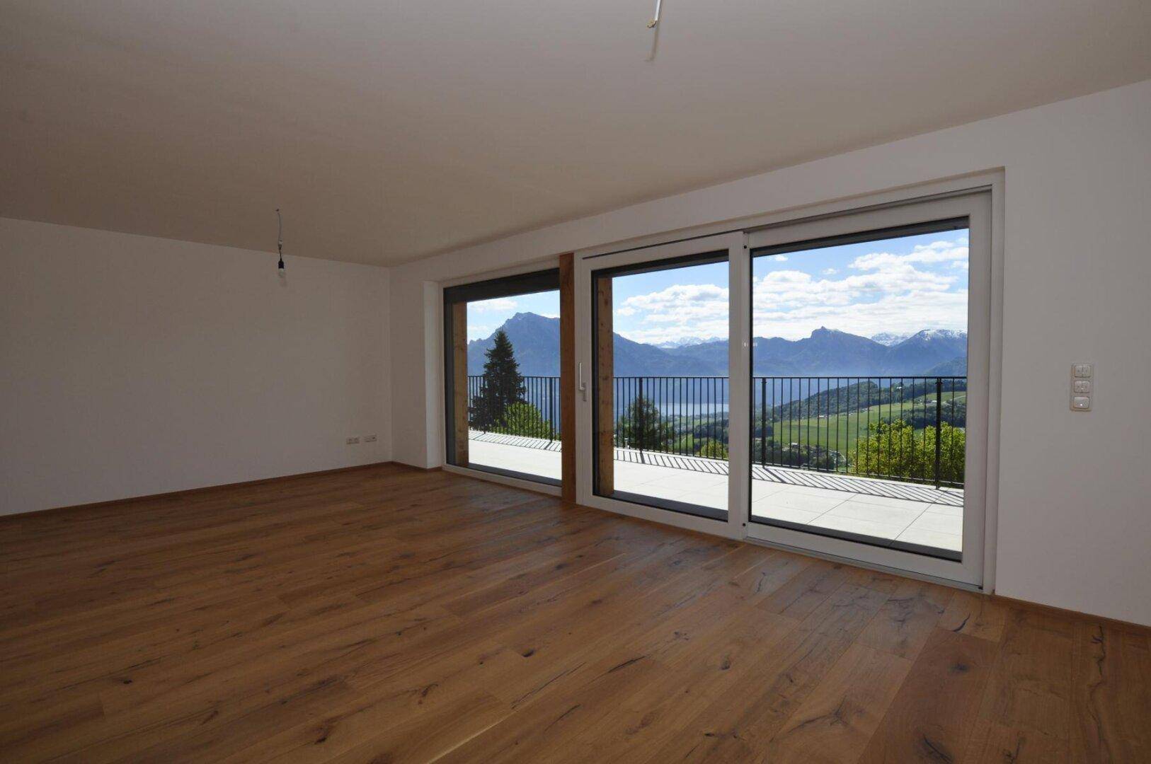 Helles Wohnzimmer mit Holzboden und großen Schiebetüren zum Balkon mit Seeblick.