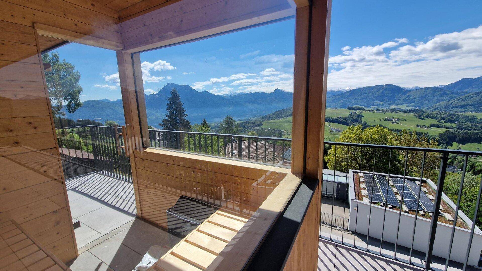 Heller Raum mit Holzverkleidung und Panoramafenstern mit Blick auf Berge und See.