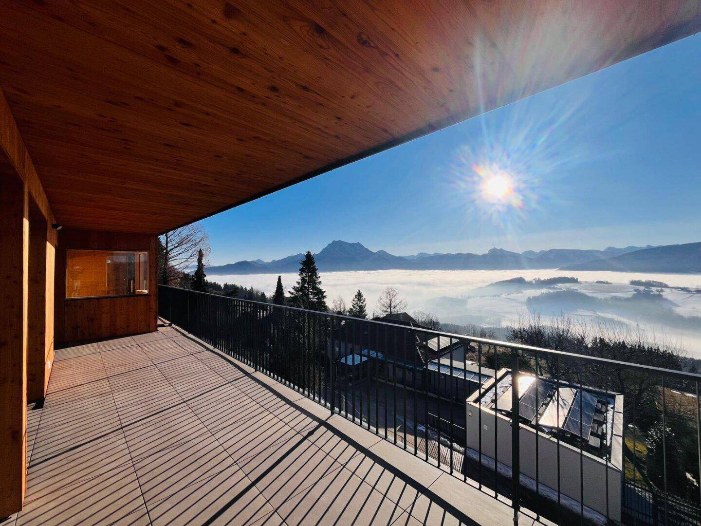 Sonniger Balkon mit Panoramablick über eine Nebellandschaft und schneebedeckte Berge.