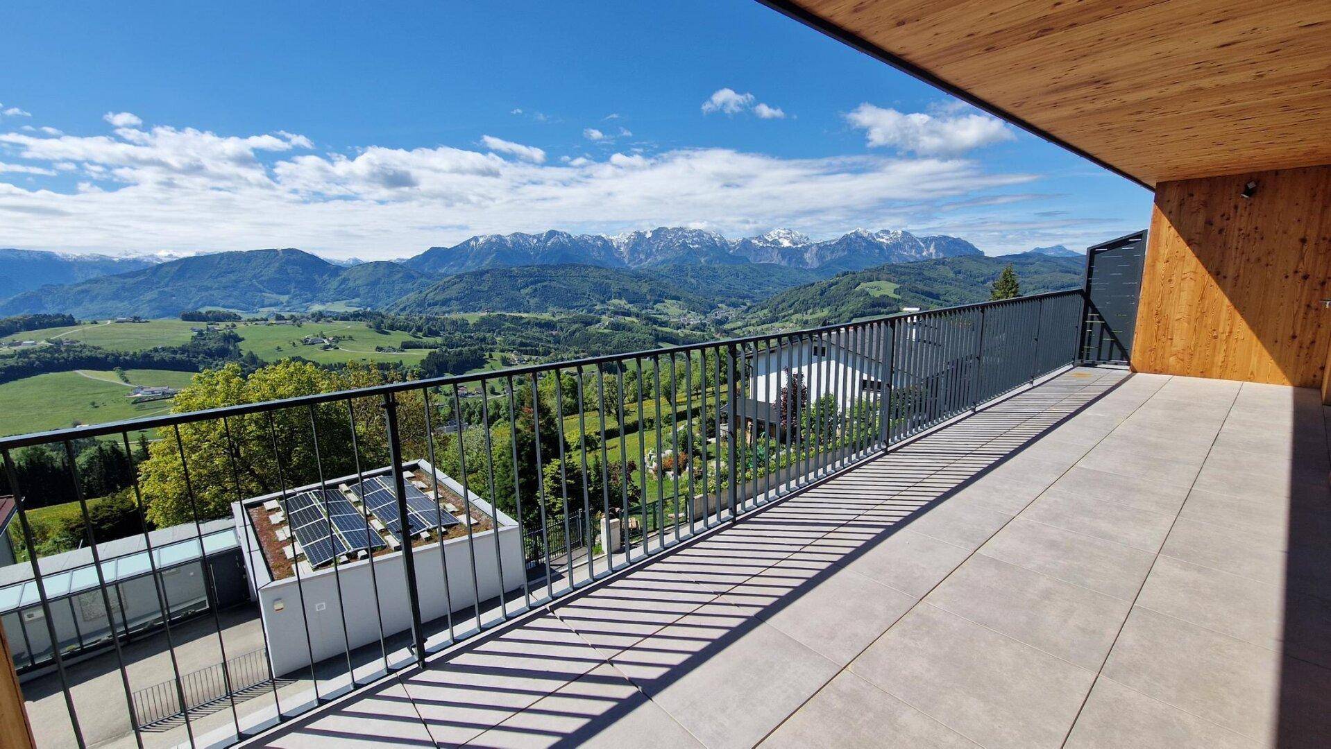 Breiter Balkon mit Fliesenboden und weitem Blick auf grüne Hügel und schneebedeckte Berge.