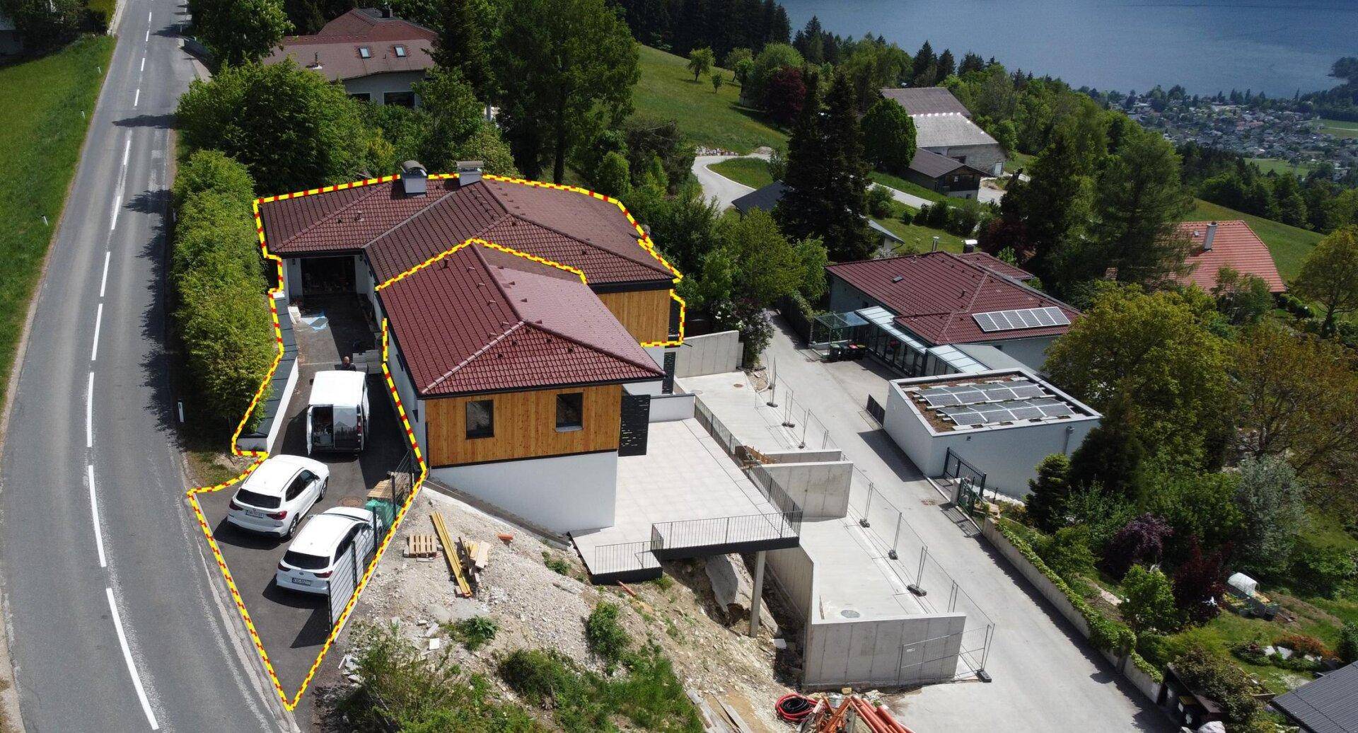 Luftaufnahme eines Neubaus mit Zufahrt, Parkplätzen und Seeblick.
