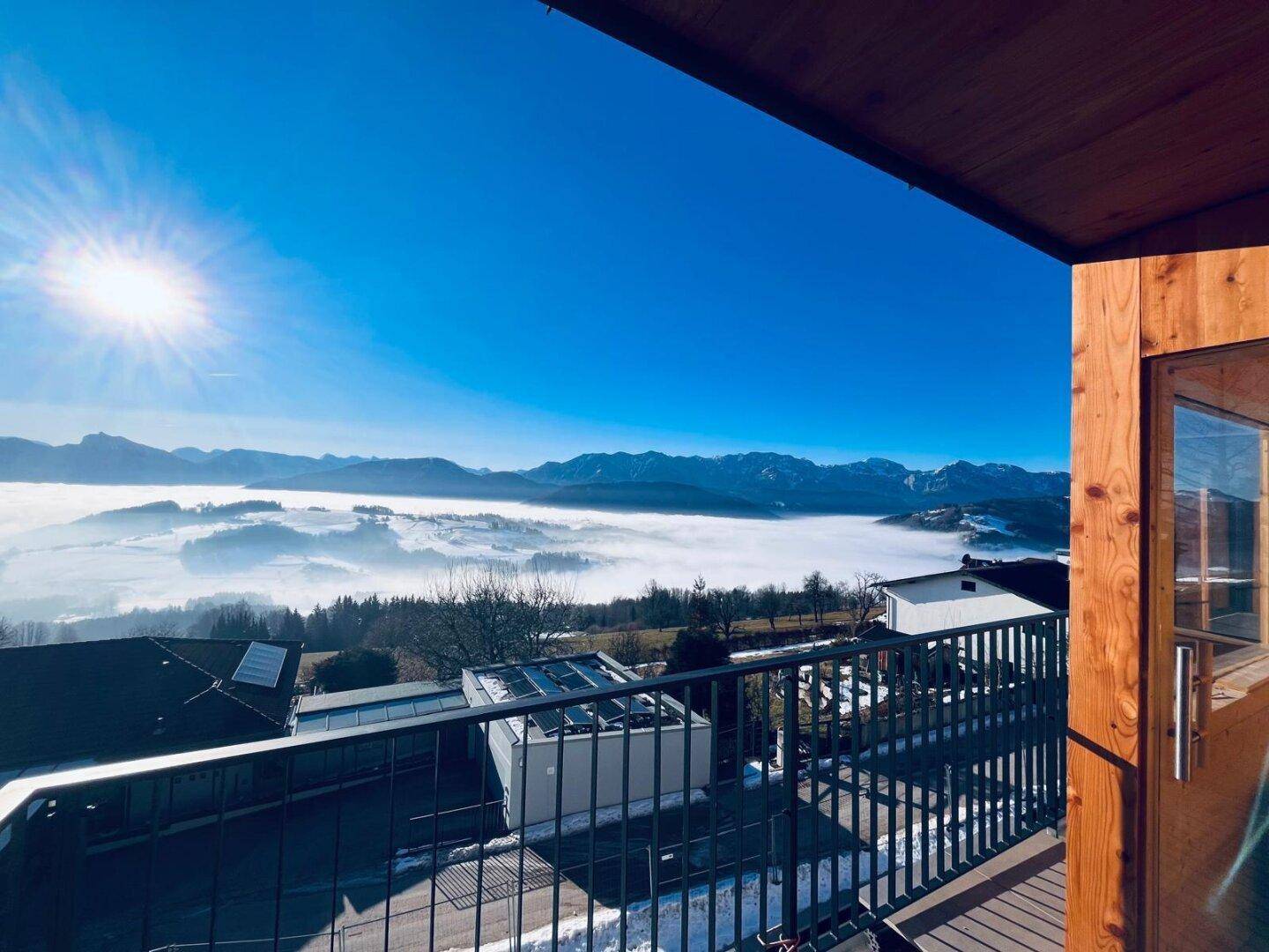 Sonniger Balkon mit Panoramablick über eine Nebellandschaft und schneebedeckte Berge.