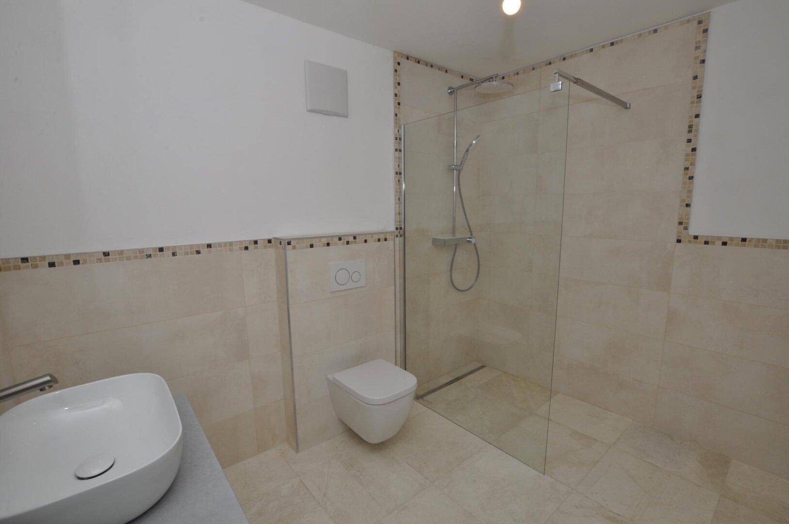 Helles Badezimmer mit begehbarer Dusche und wandhängendem WC, gefliest in neutralen Farbtönen.