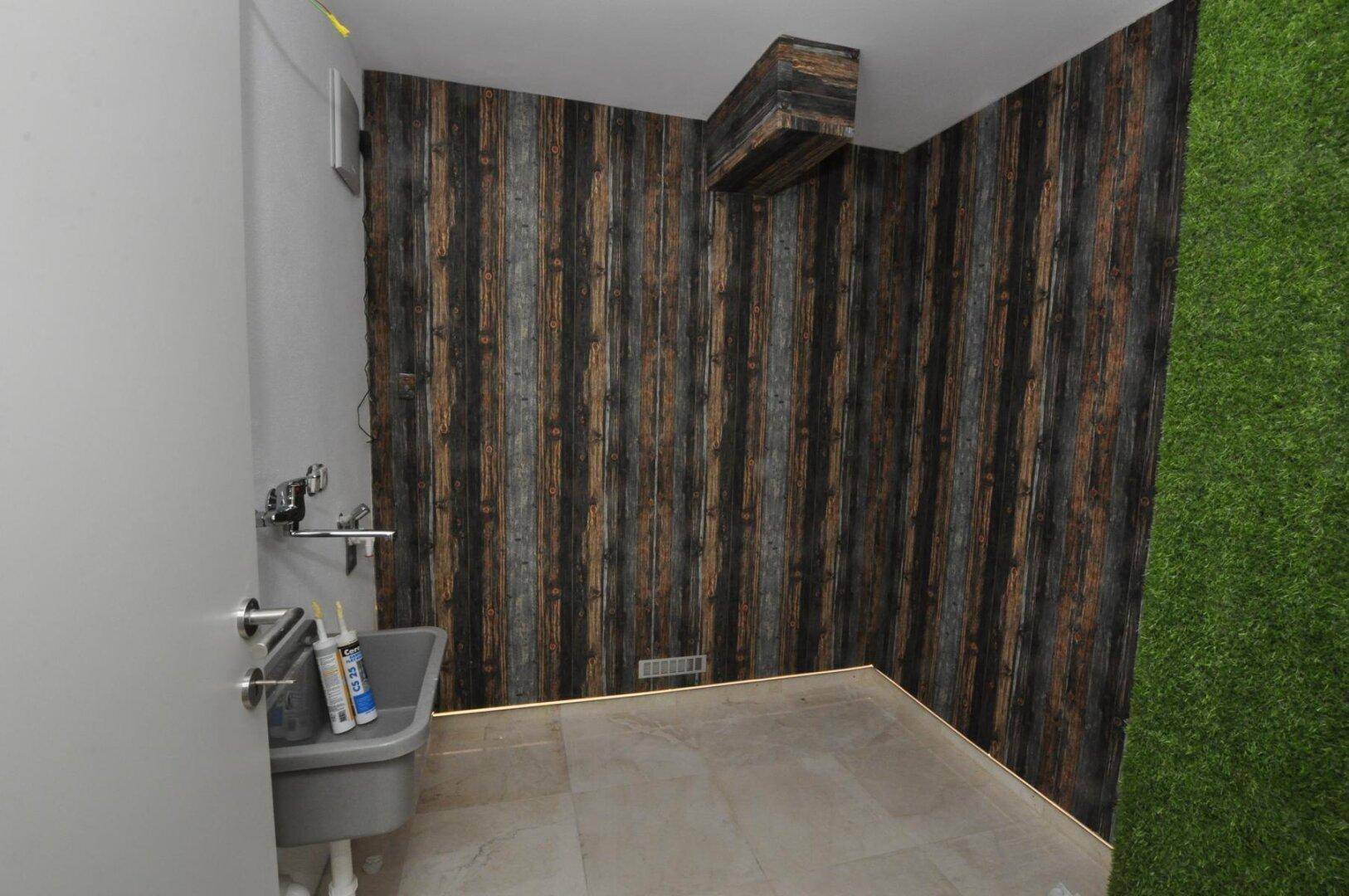Abstellraum mit Waschbecken und dekorativer Wandverkleidung, teilweise mit Kunstrasen.