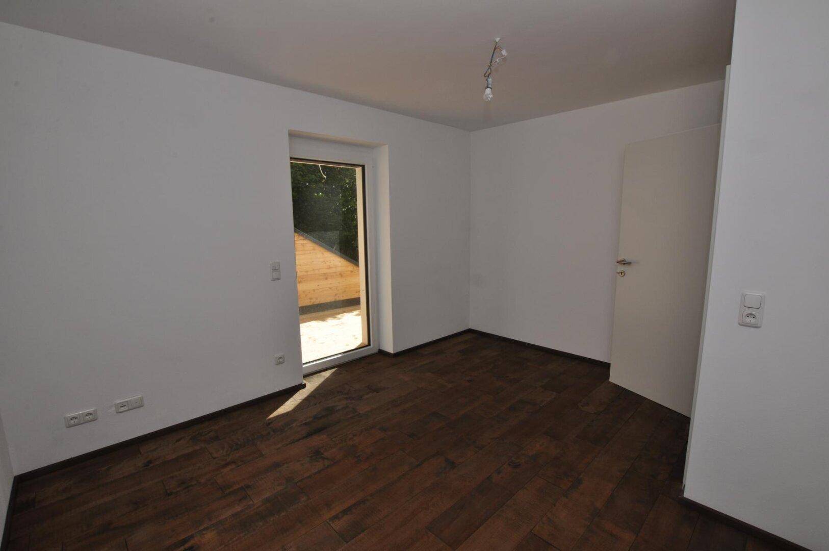 Schlafzimmer mit Holzboden und Zugang zu einem Außenbereich, hell und unmöbliert.