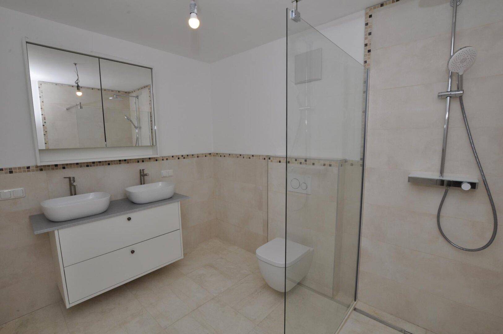 Modernes Badezimmer mit Doppelwaschbecken, wandhängendem WC und großer begehbarer Dusche.