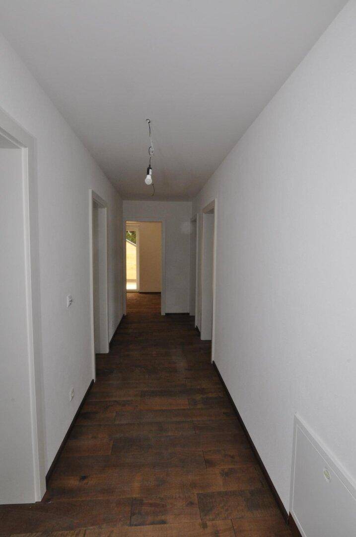Langer Flur mit Holzboden und mehreren Türen, der zu verschiedenen Räumen führt.