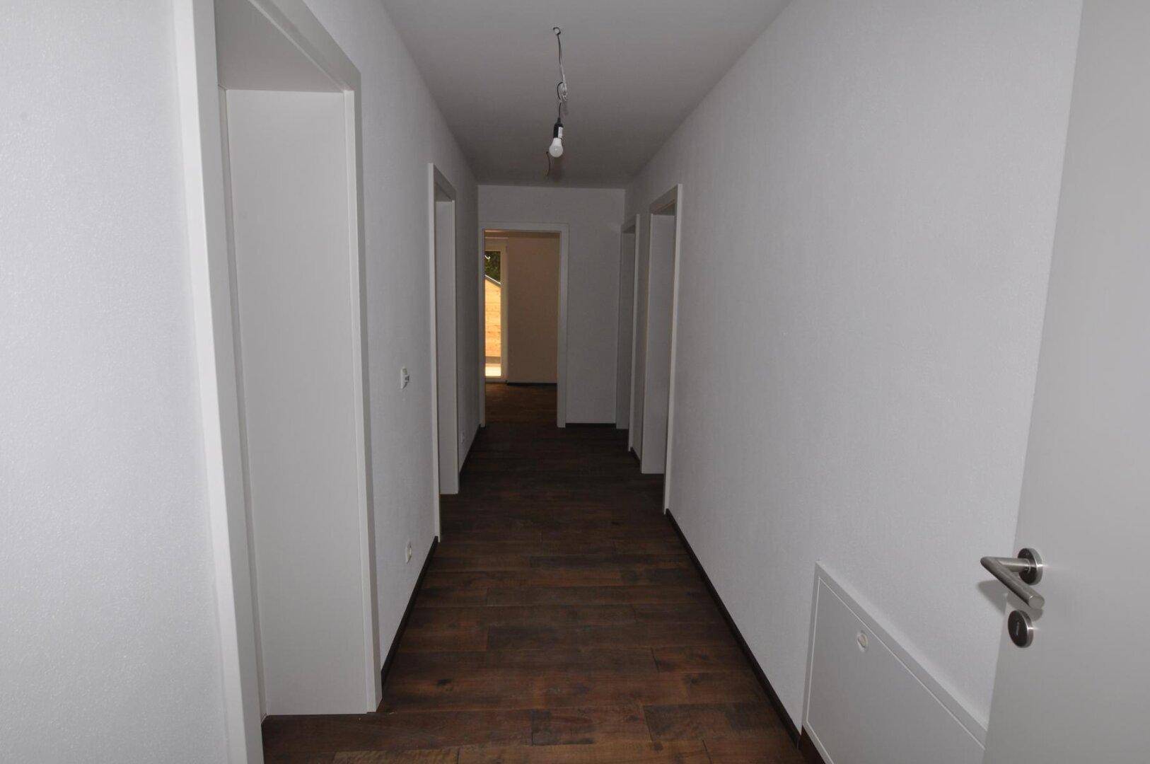 Schlichter Flur mit Holzboden und weißen Wänden, der zu den angrenzenden Zimmern führt.