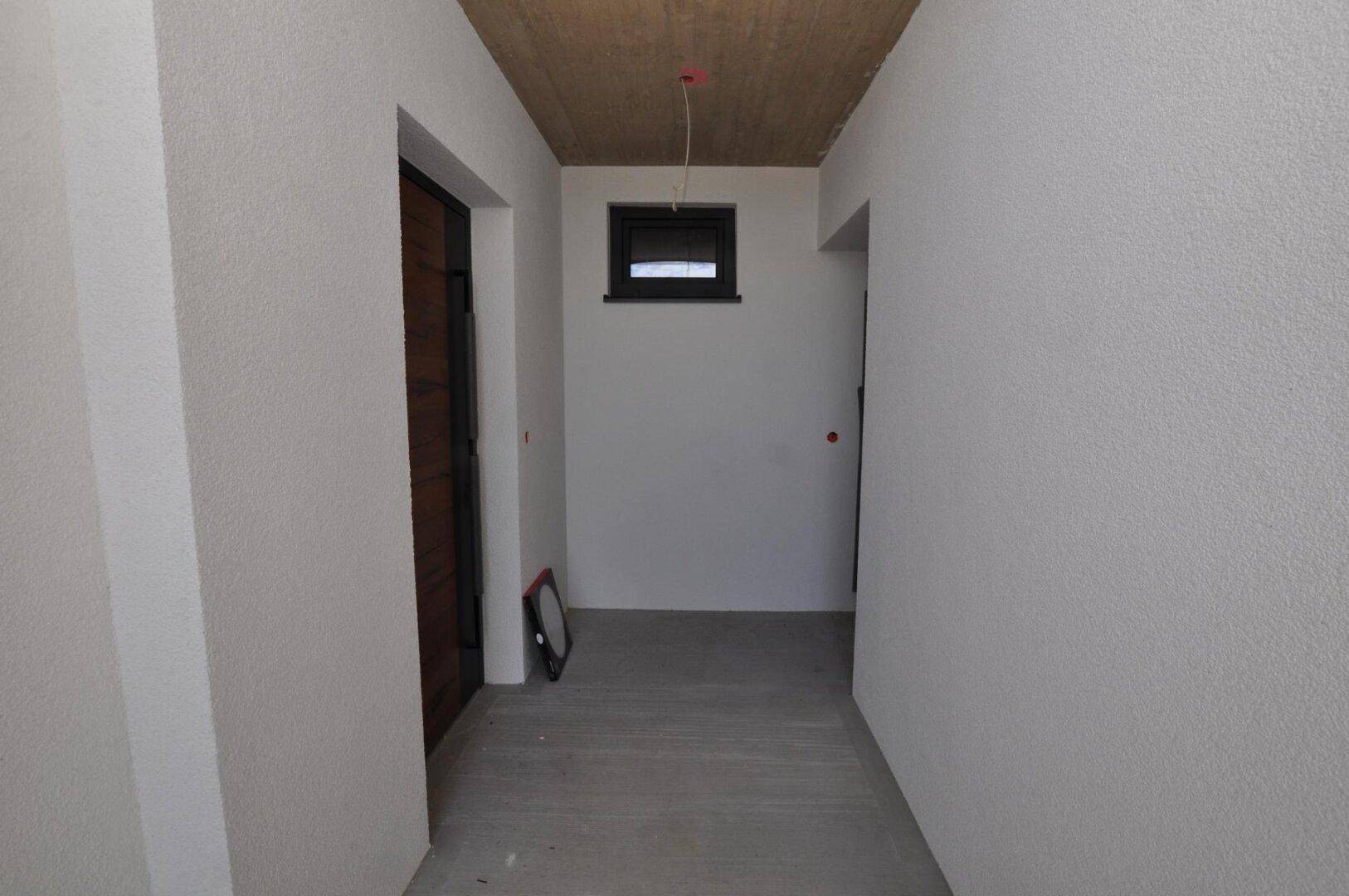 Eingangsbereich mit schlichten Wänden und einem kleinen Fenster, das Tageslicht hereinlässt.