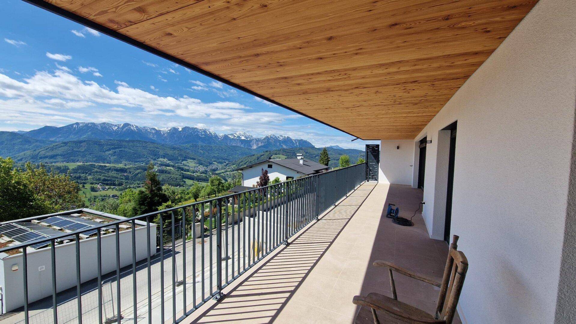 Langer Balkon mit Holzdach und beeindruckendem Blick auf die schneebedeckten Berge.