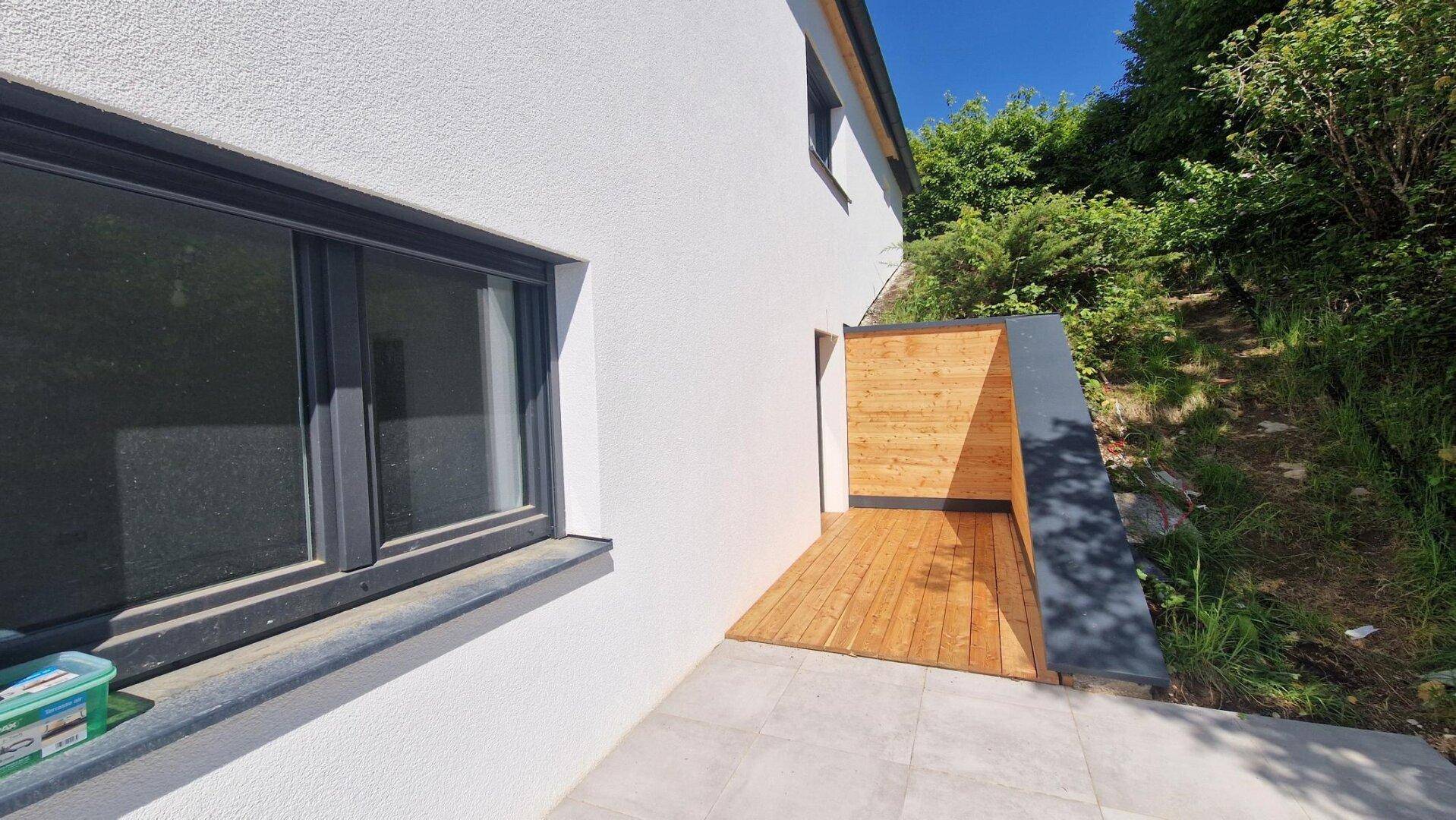 Kleine Terrasse mit Holzboden und Zugang zum Gartenbereich, umgeben von Grün.