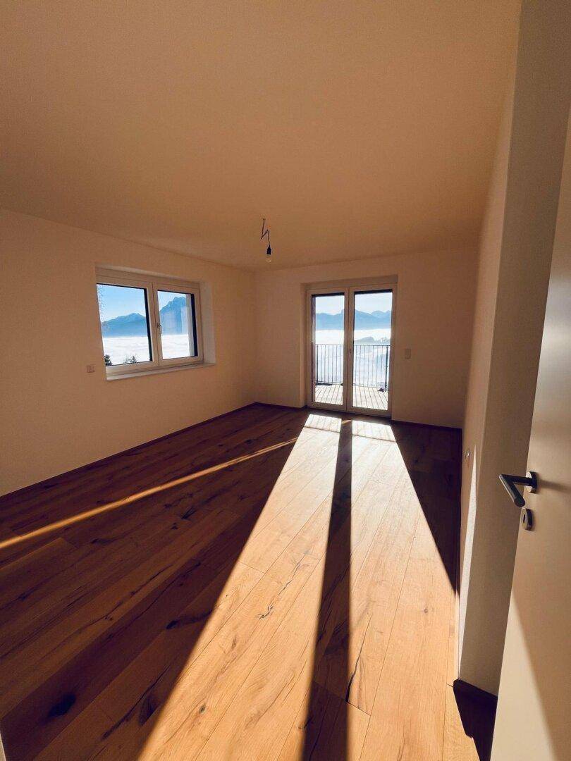 Helles Schlafzimmer mit Holzboden und großen Fenstern, die viel Sonnenlicht hereinlassen.