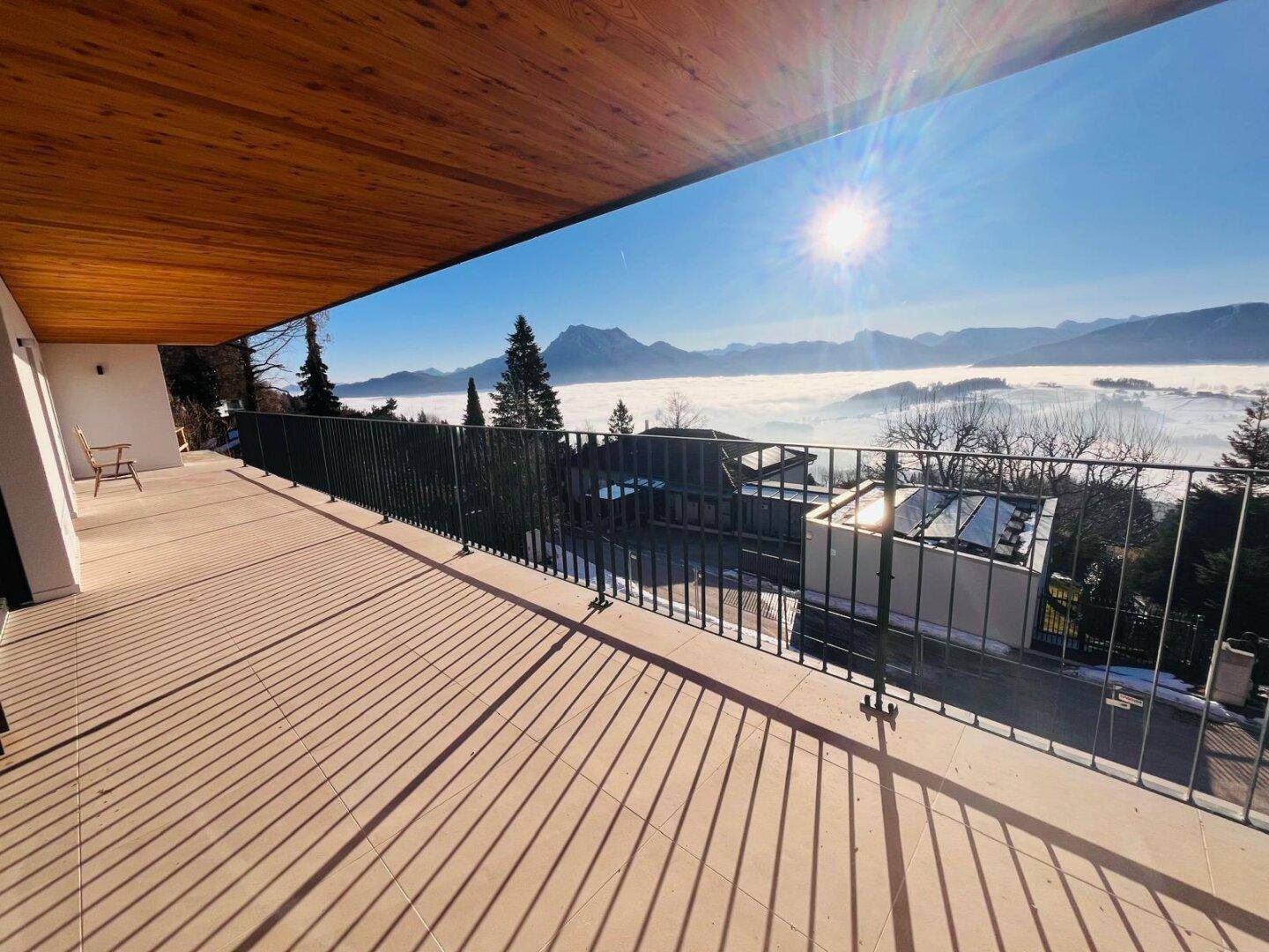 Geräumiger Balkon mit Holzdach und sonnigem Blick auf die Berge und eine Nebellandschaft.