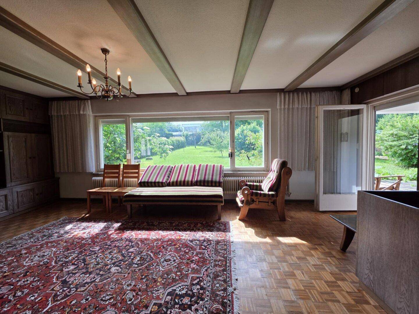 Helles Wohnzimmer mit Eichenparkett, Holzbalkendecke und weitem Blick in den grünen Garten.