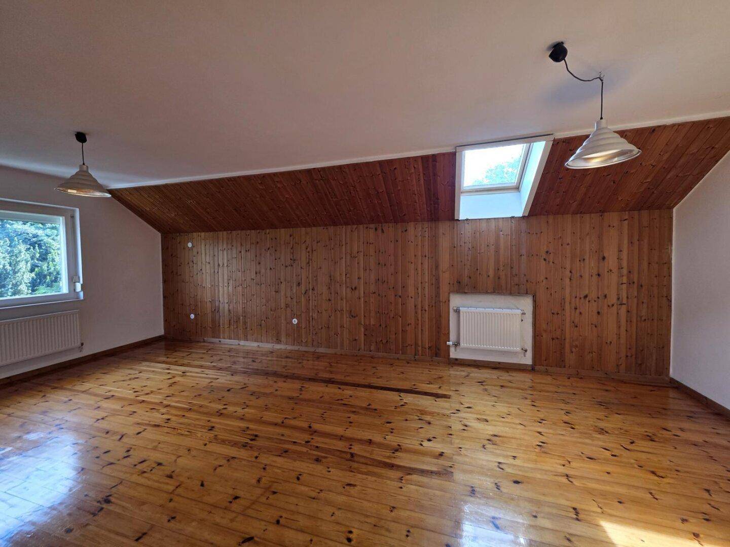 Geräumiger Dachbodenraum mit Holzboden, Holzvertäfelung und Fenstern für viel Tageslicht.
