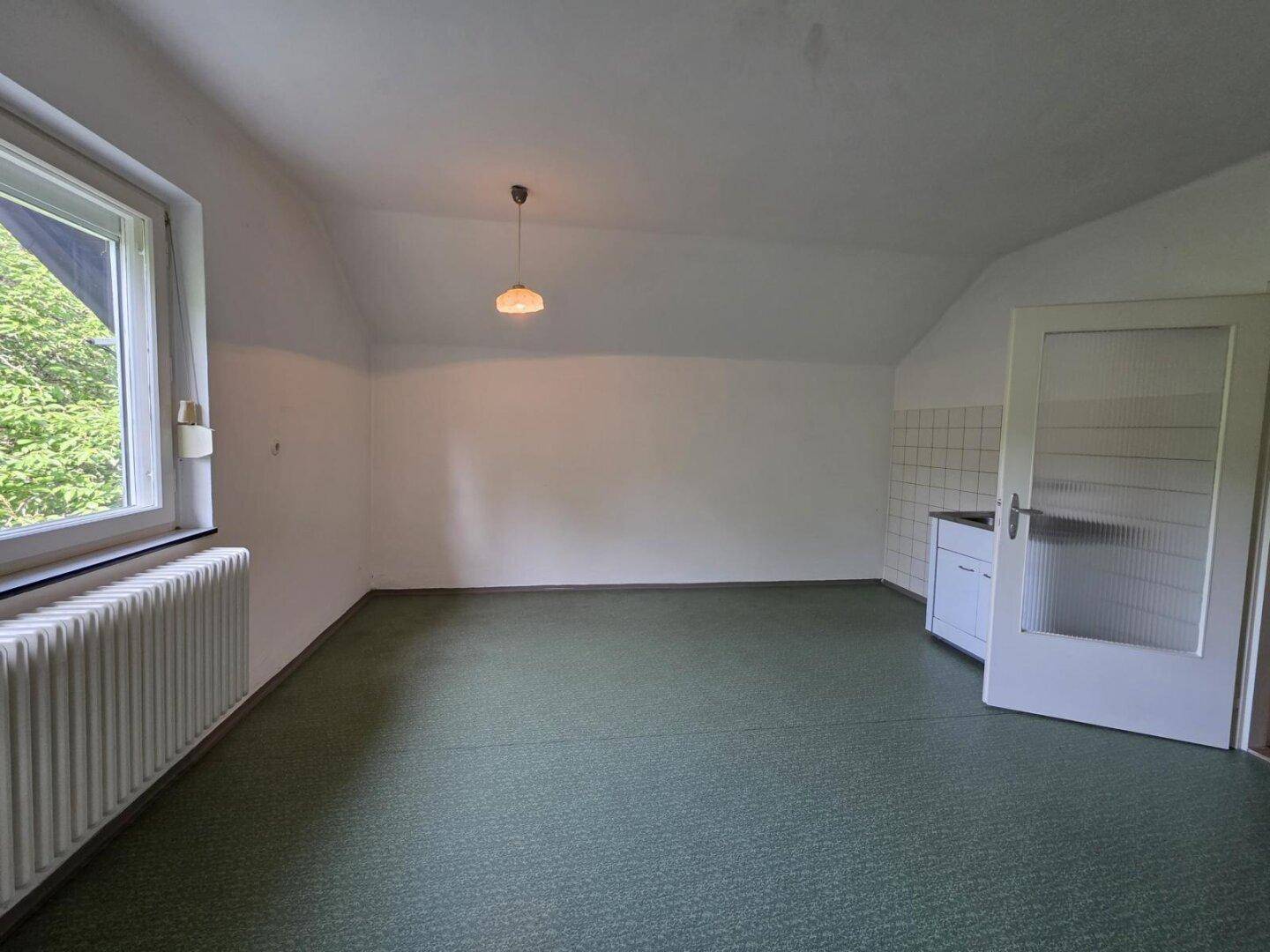 Helles Zimmer mit grünem Boden, Fenster und einem kleinen Küchenbereich mit Spüle.