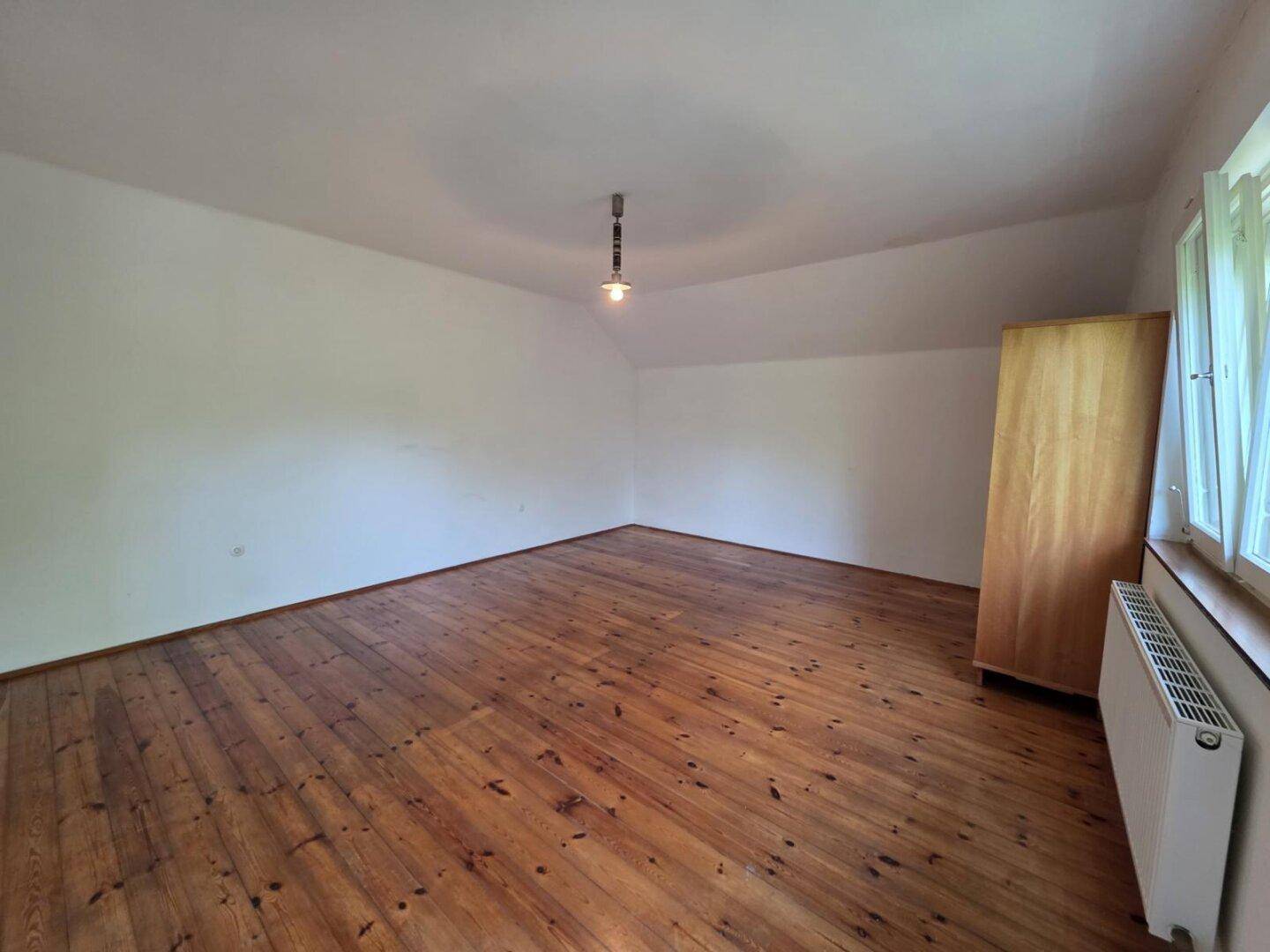 Leeres Schlafzimmer mit Holzboden, weißen Wänden und einem Fenster für natürliches Licht.