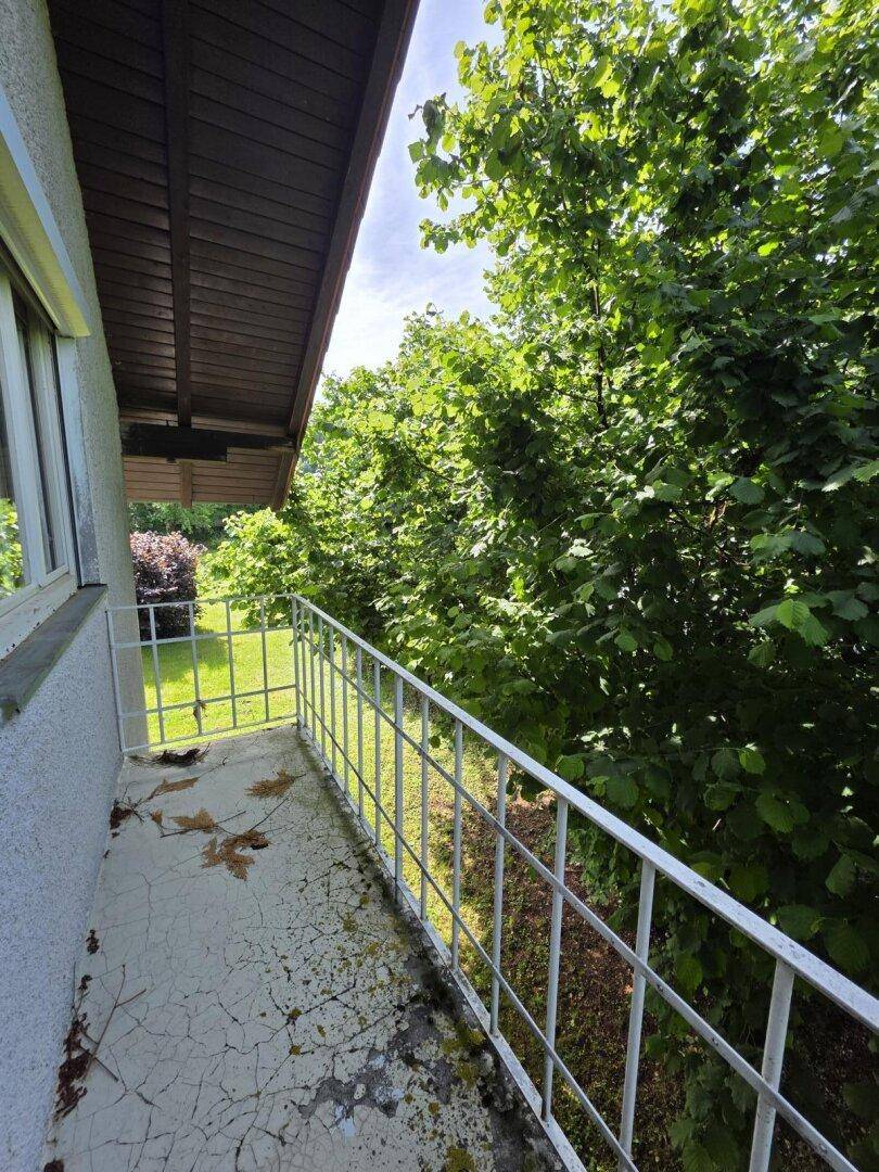 Schmaler Balkon mit weißem Geländer und Blick ins dichte Grün der Bäume.