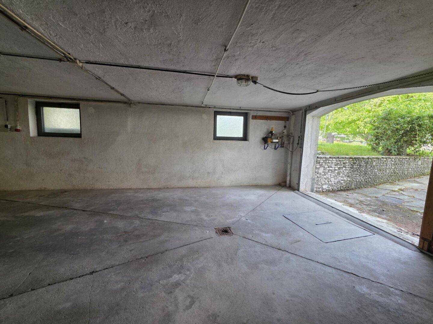 Geräumige Garage mit Betonboden und kleinen Fenstern, offen zum Außenbereich.