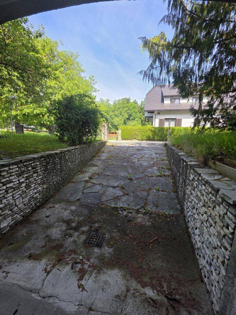 Einfahrt mit Steinmauern, die zur Garage führt, mit einem Haus im Hintergrund.