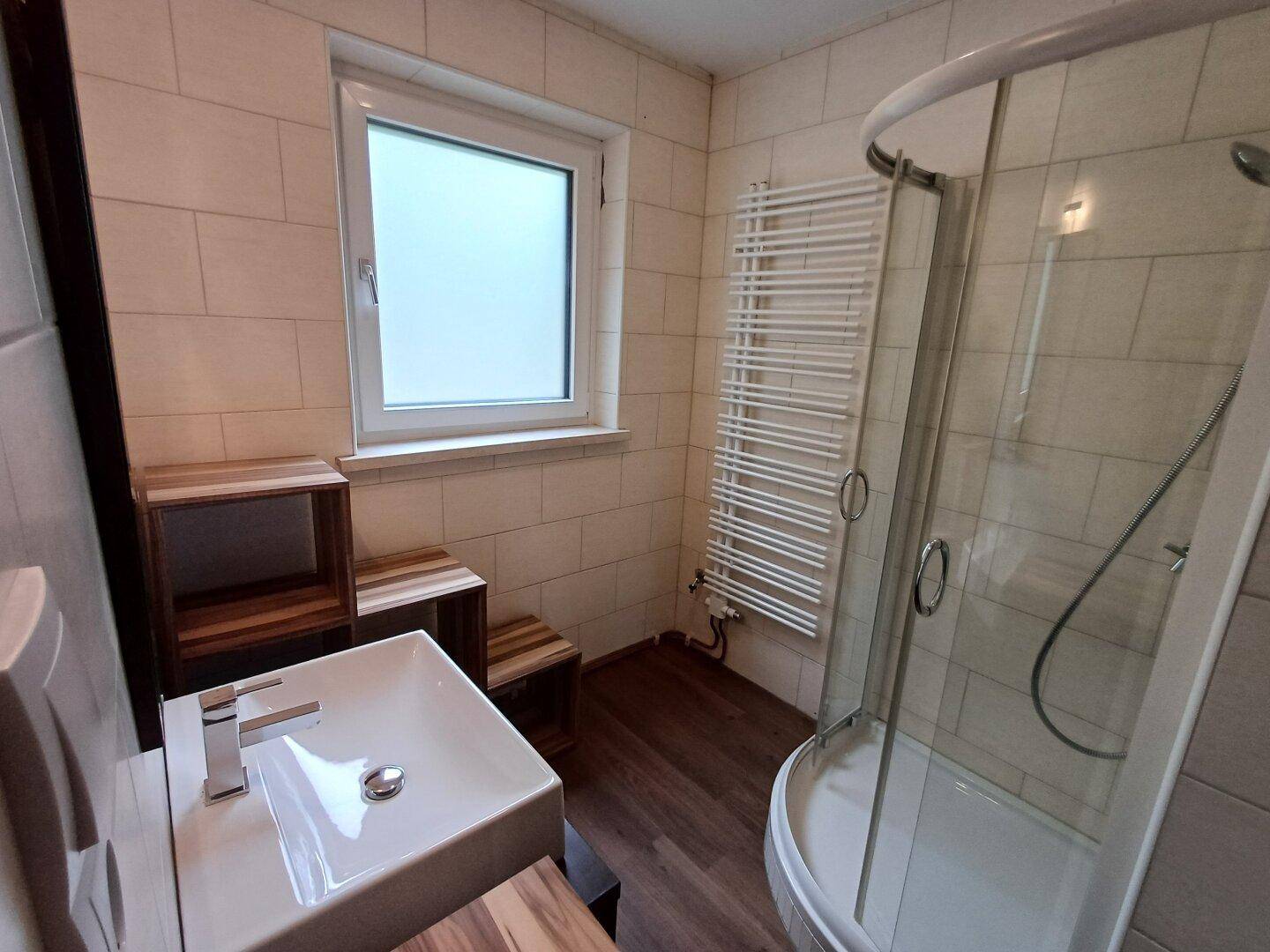 Modernes Badezimmer mit Duschkabine, Fliesenwänden, Einzelwaschbecken und beheiztem Handtuchhalter.
