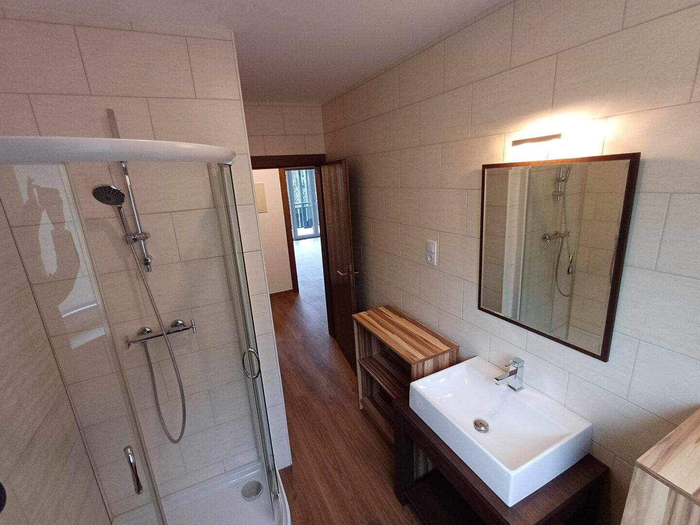 Funktionales Badezimmer mit Duschbereich, modernem Waschbecken und einem Spiegel über dem Waschtisch.