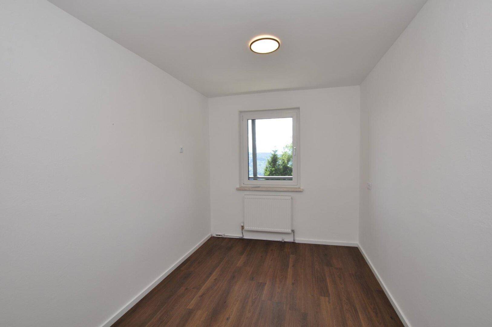 Kleines, helles Zimmer mit Holzboden und einem Fenster, ideal als Schlaf- oder Arbeitszimmer.