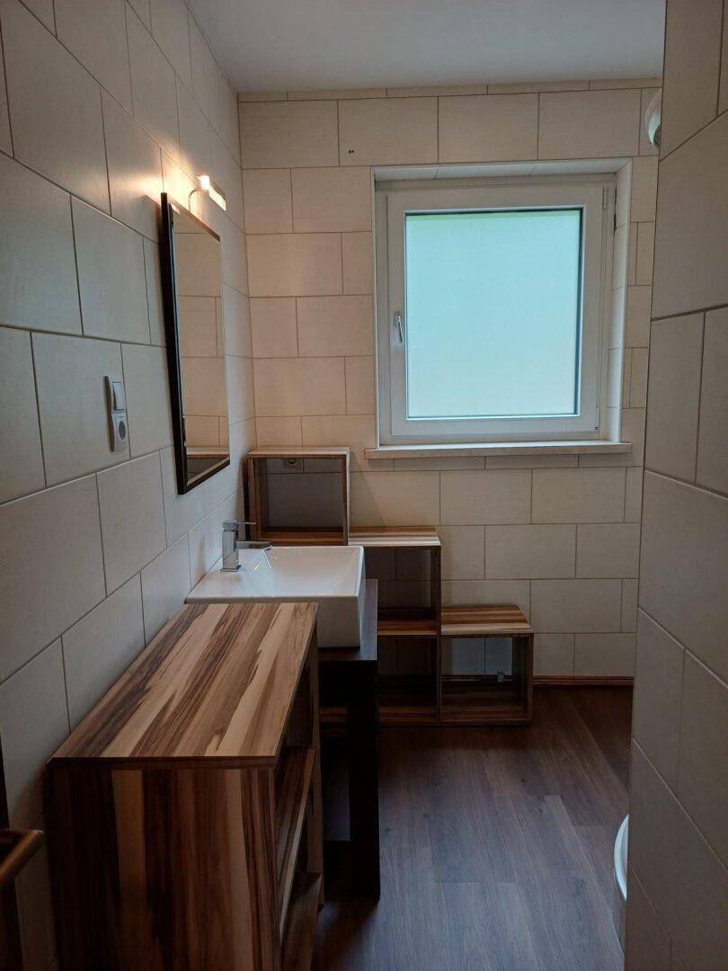Helles Badezimmer mit beigefarbenen Fliesen, modernem Waschbecken und einem Fenster für Tageslicht.