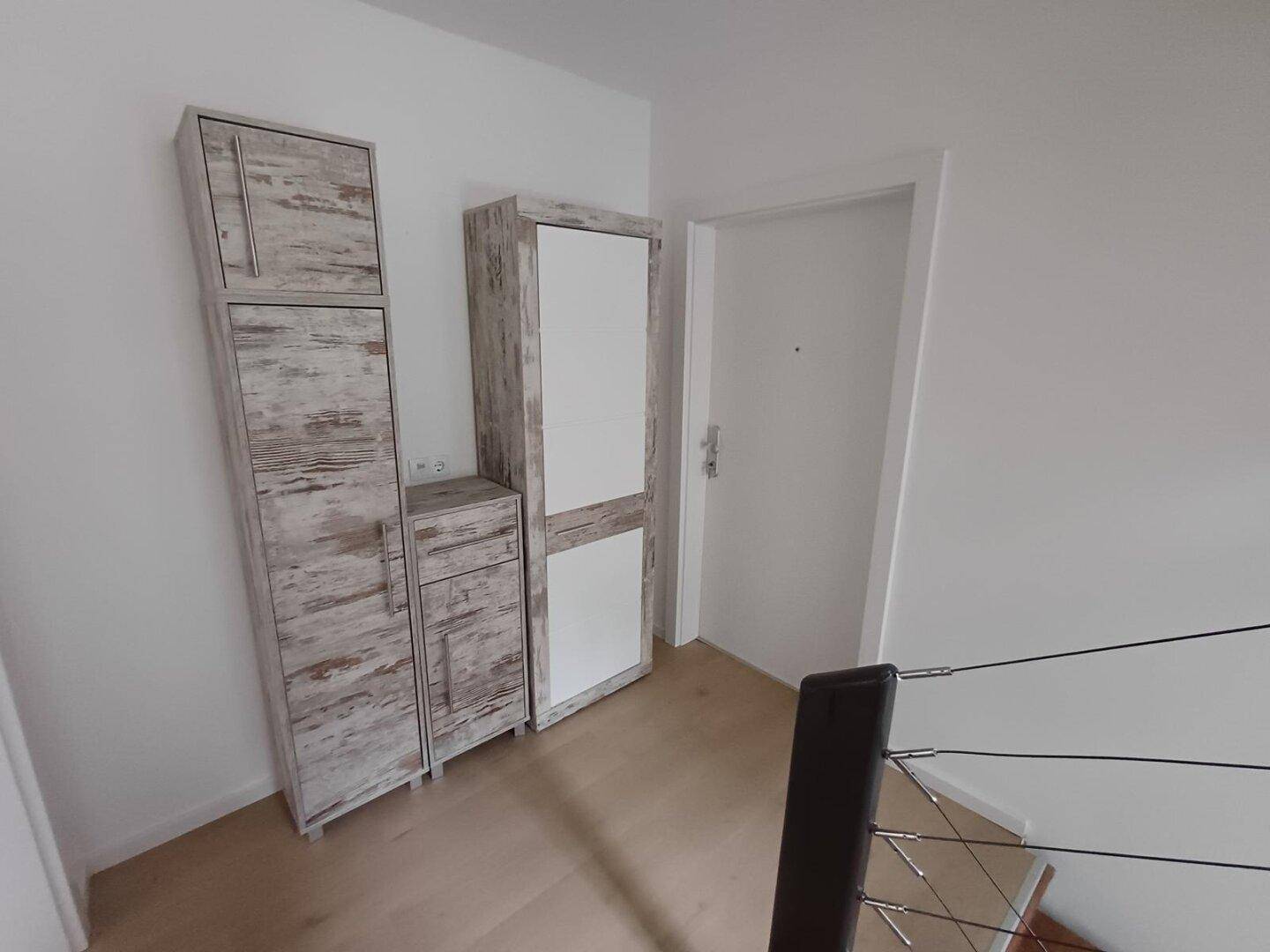 Eingangsbereich mit rustikalen Holzschränken und einer modernen weißen Tür.