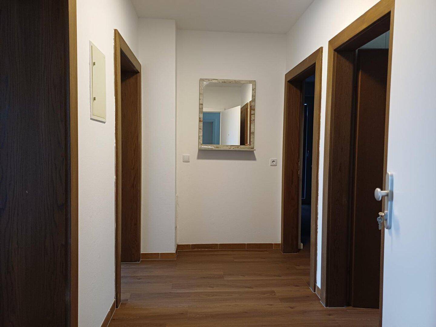 Heller Flur mit dunklem Holzboden, weißen Wänden und mehreren Türen, die zu den angrenzenden Räumen führen.