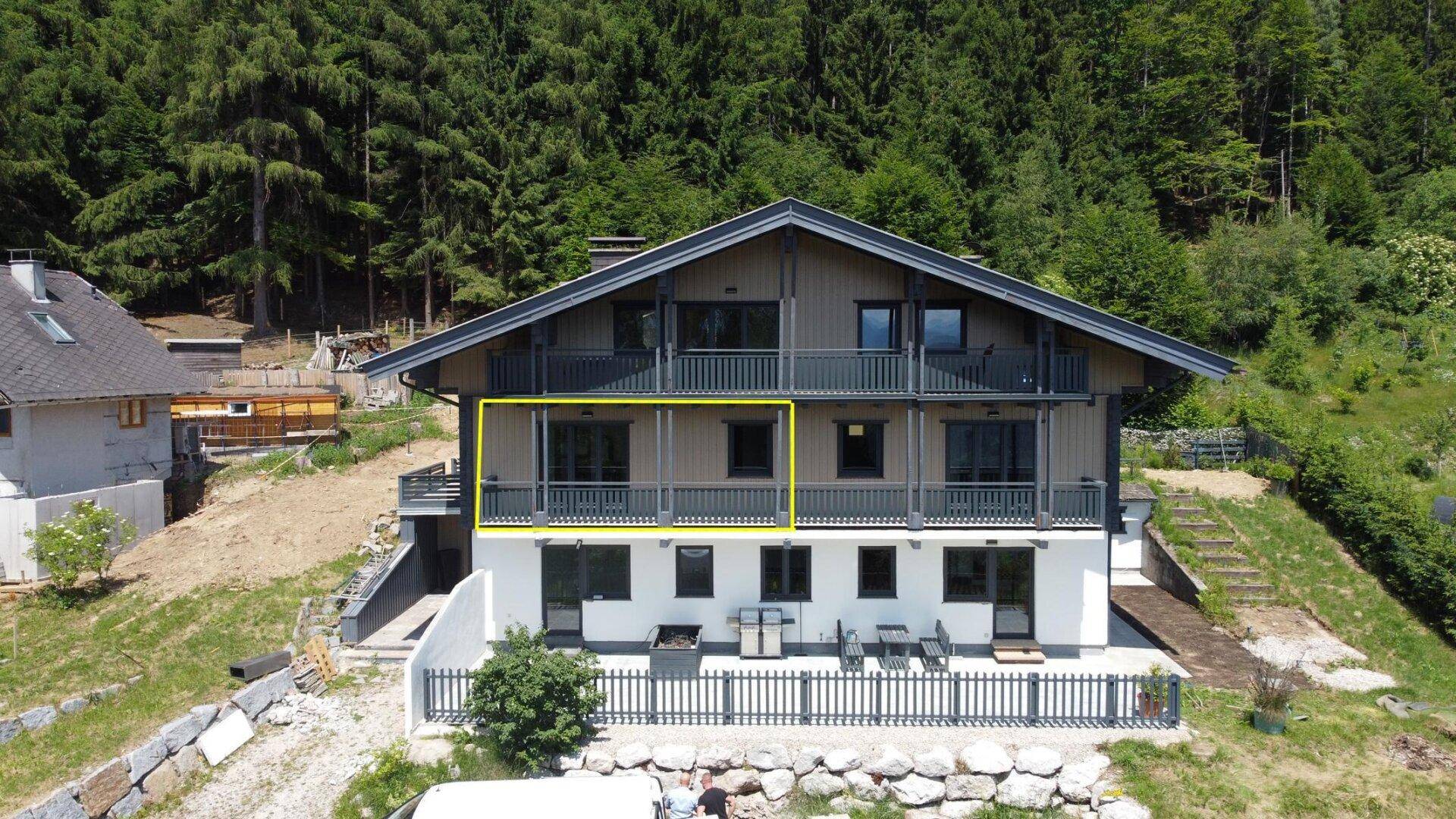 Modernes Wohnhaus mit mehreren Balkonen und einer Terrasse, eingebettet in eine grüne Hügellandschaft.